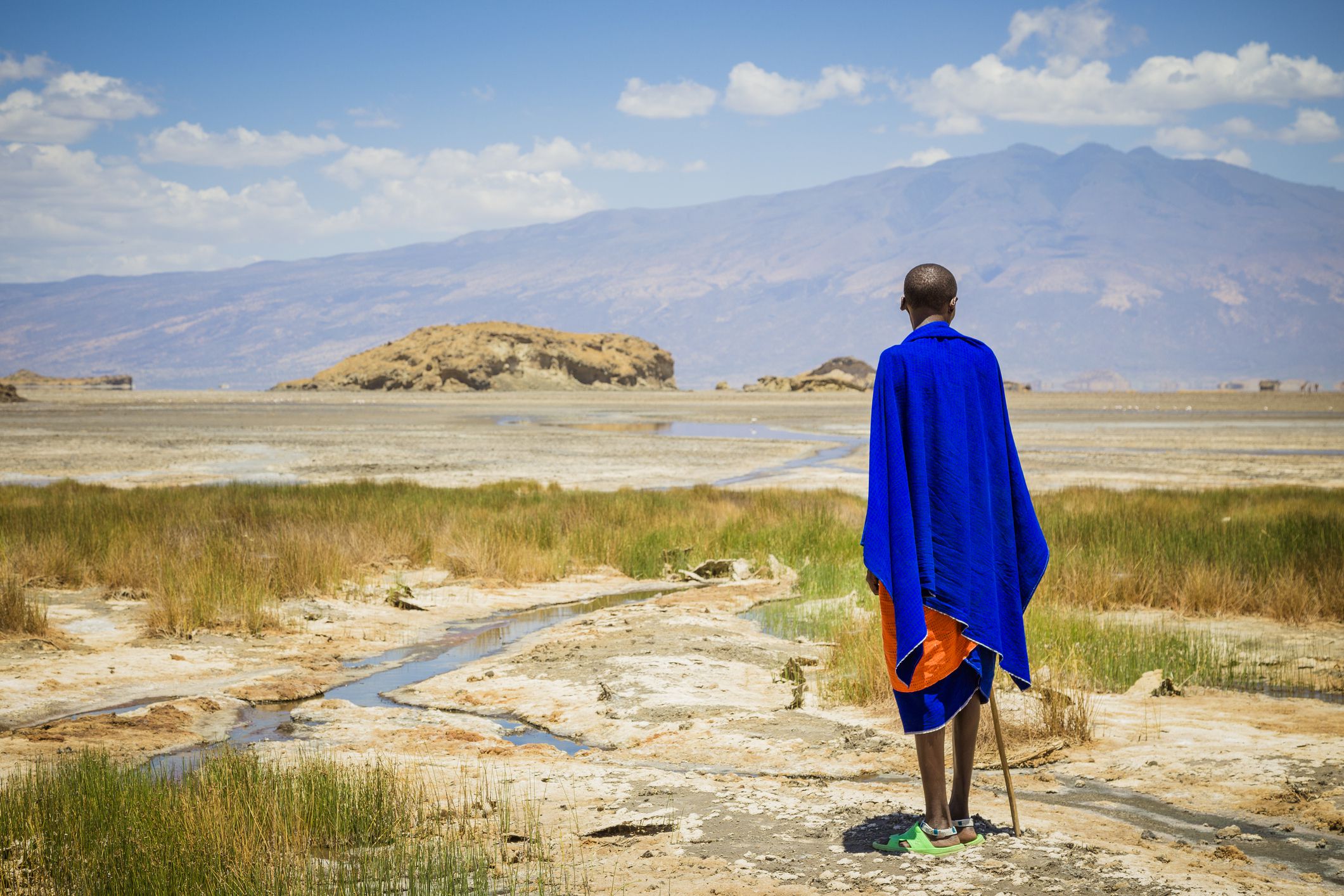 Lake Natron, Tanzania - October 04, 2013: Maasai man is standing at Lake Natron in Tanzania. He looks at the salt lake on the horizon where a herd of giraffes running across the lake.