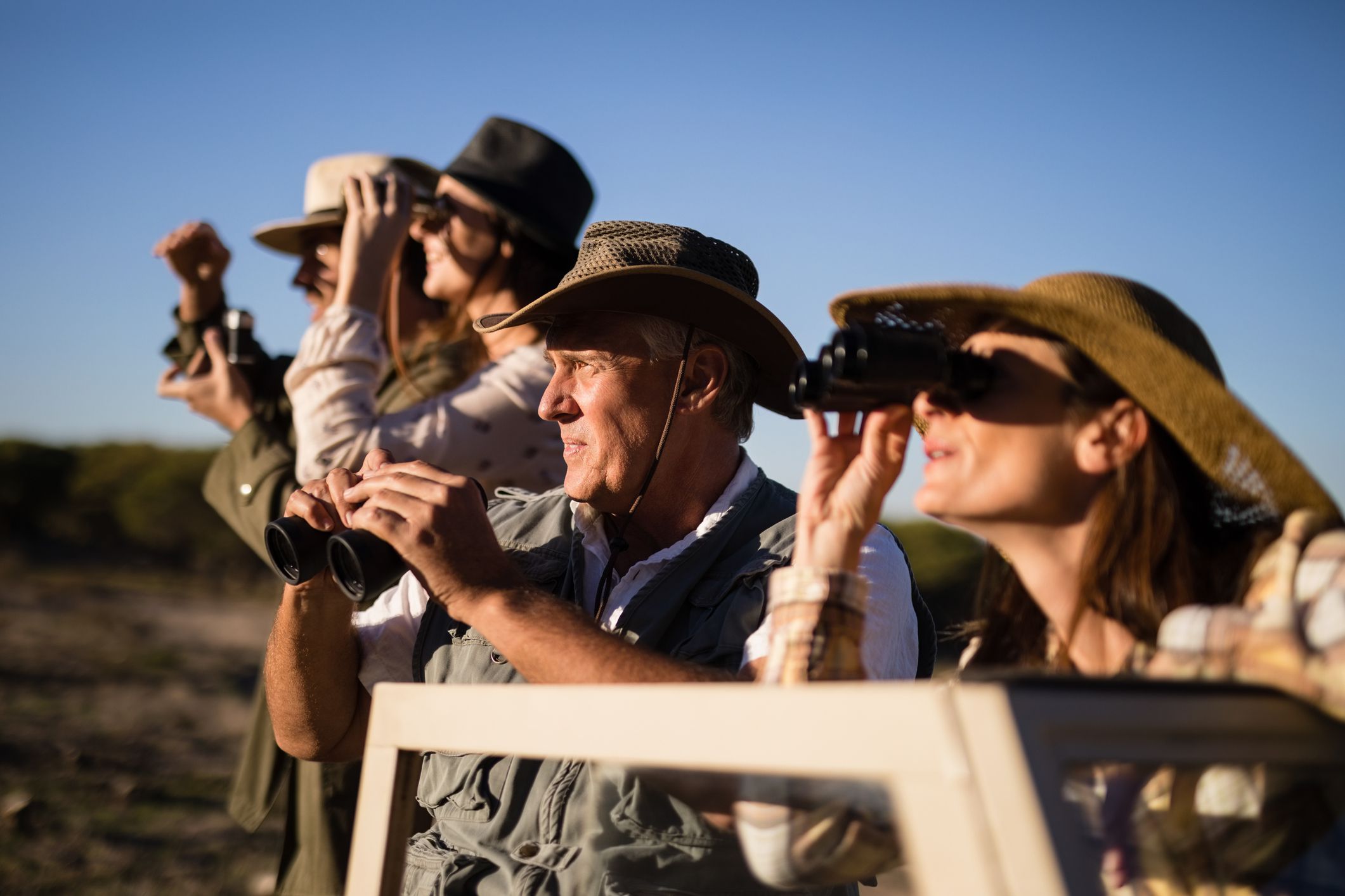 Friends looking through binoculars during safari vacation on a sunny day