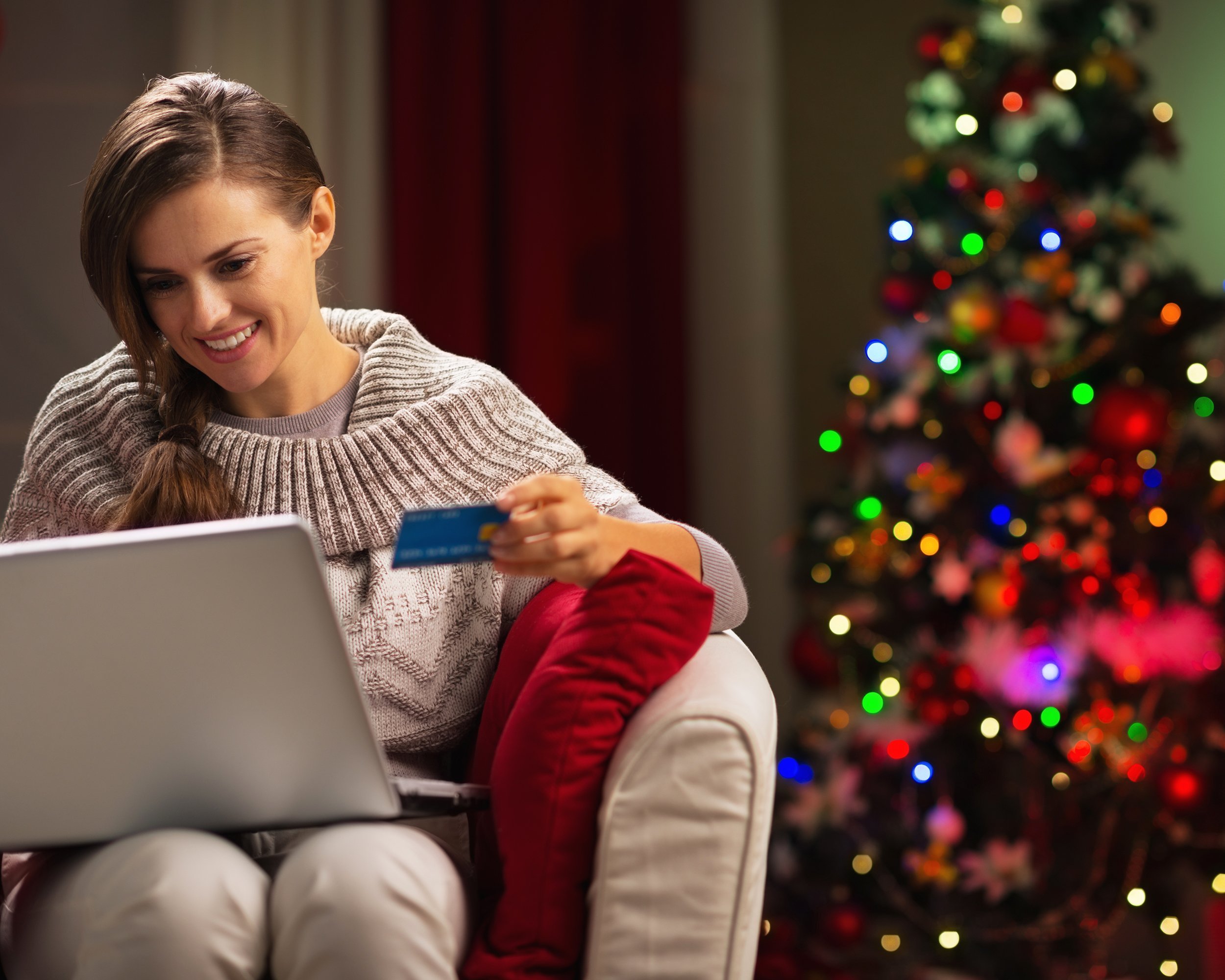 happy woman with laptop and credit card in front of Christmas tree