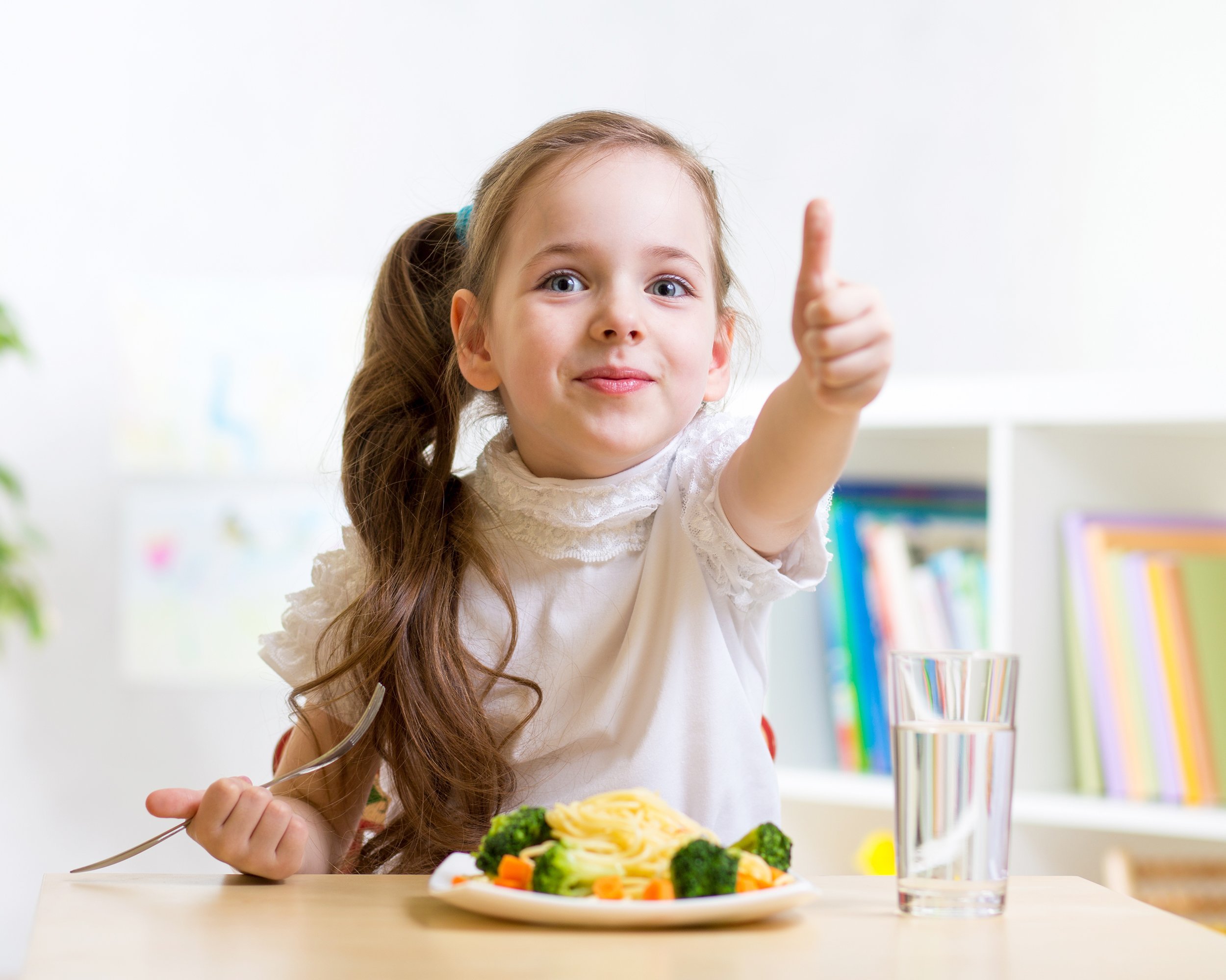 child girl eats healthy food showing thumb up at kindergarten