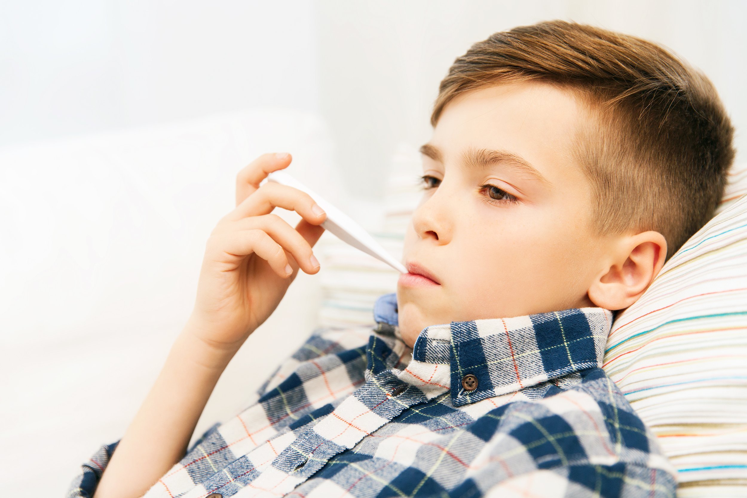 ill boy with flu measuring temperature by thermometer at home
