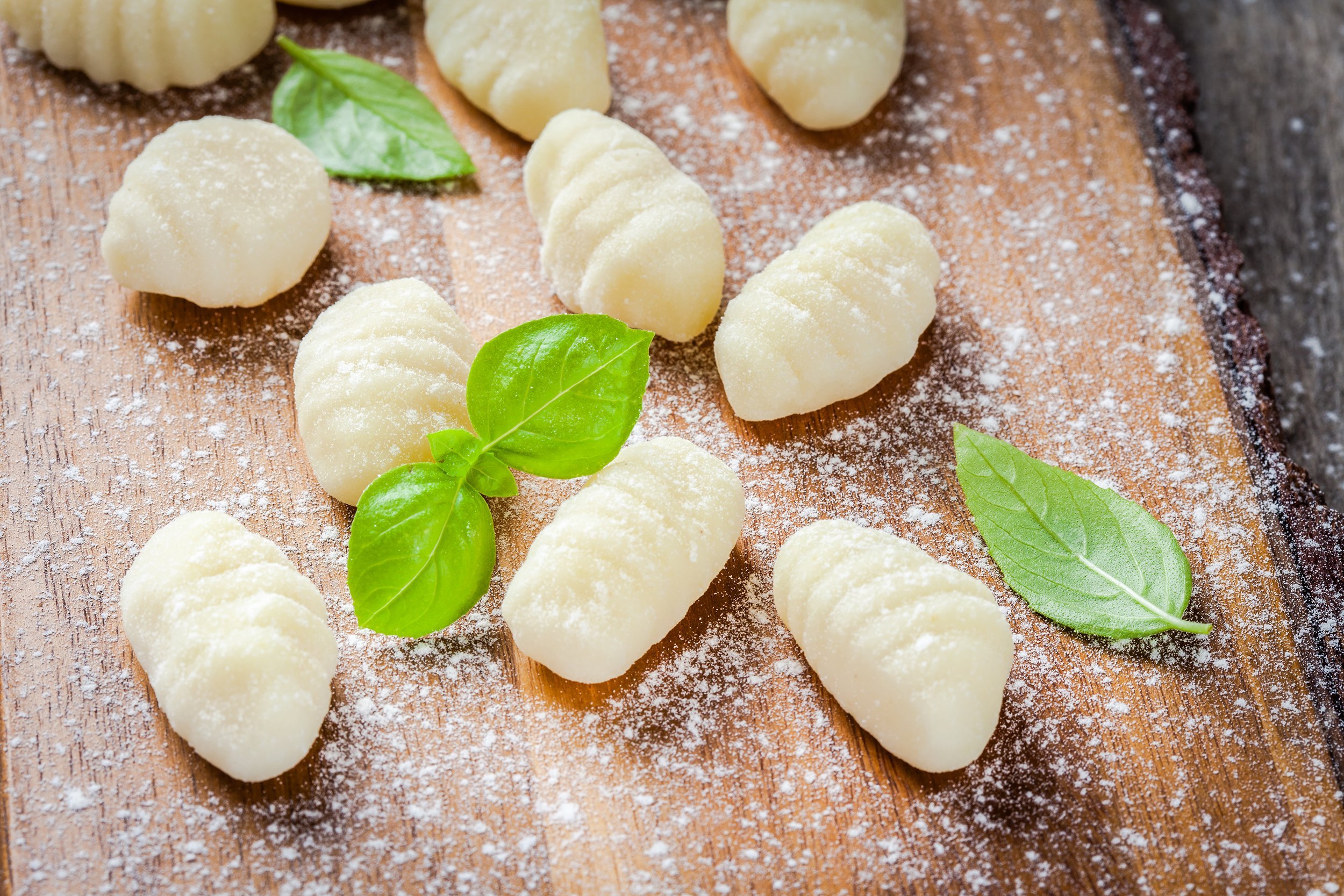 homemade raw gnocchi with flour and fresh basil on a wooden cutting board