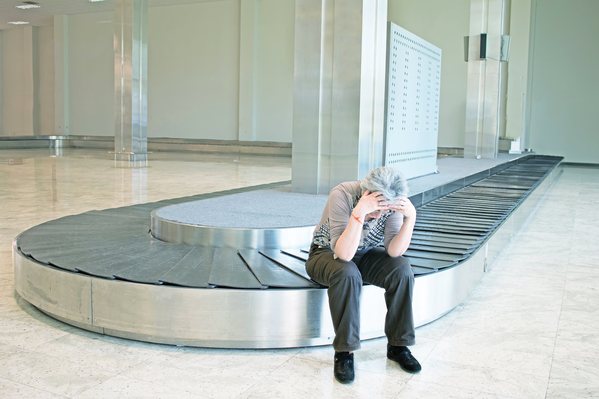 frustrated woman with lost luggage look upset sitting at the baggage carousel at an airport