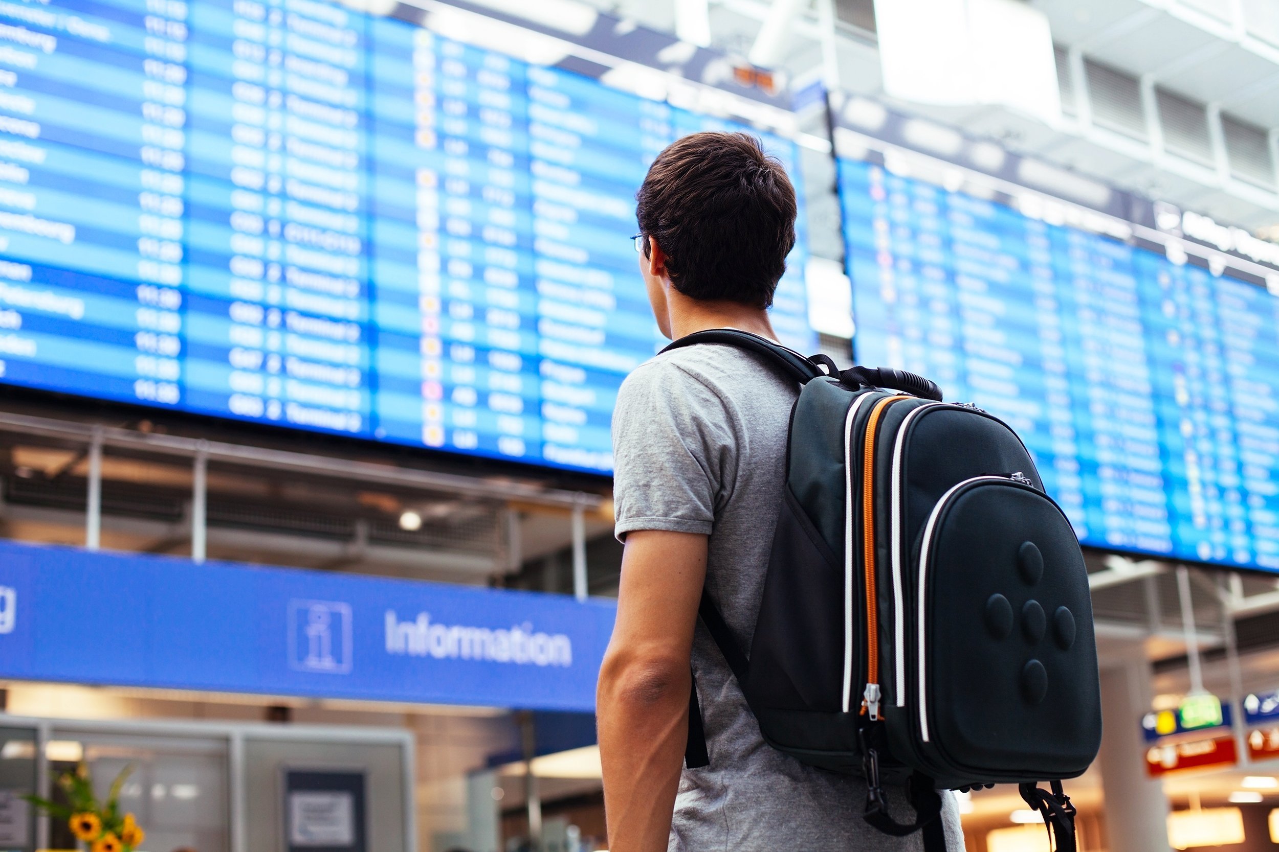 man with backpack in airport near flight timetable