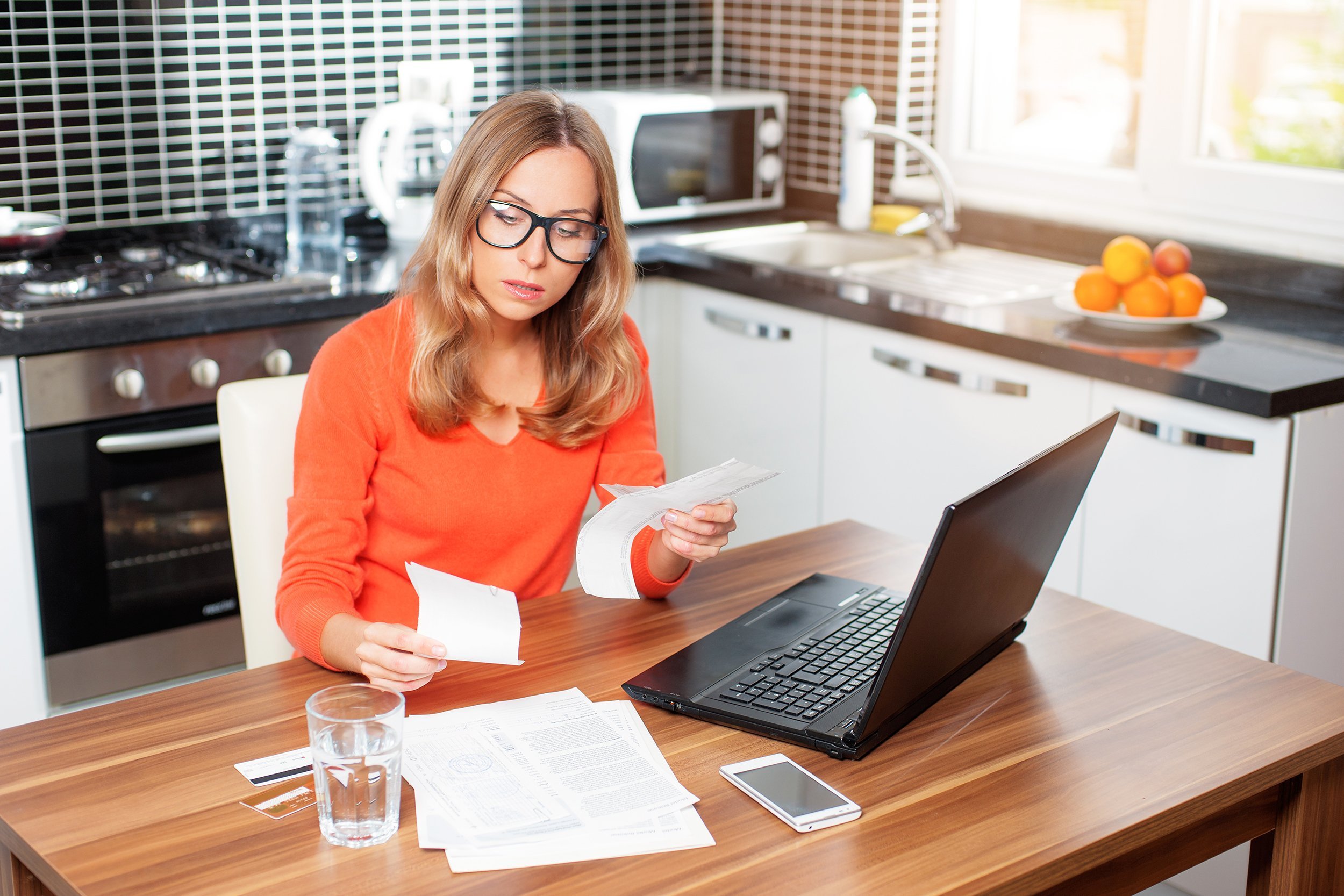 woman budgeting in her kitchen with laptop and bills