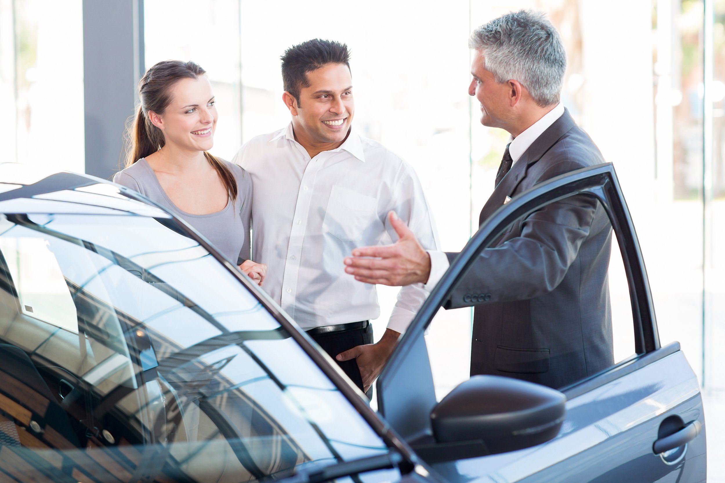 mature salesman showing new car to a couple in showroom