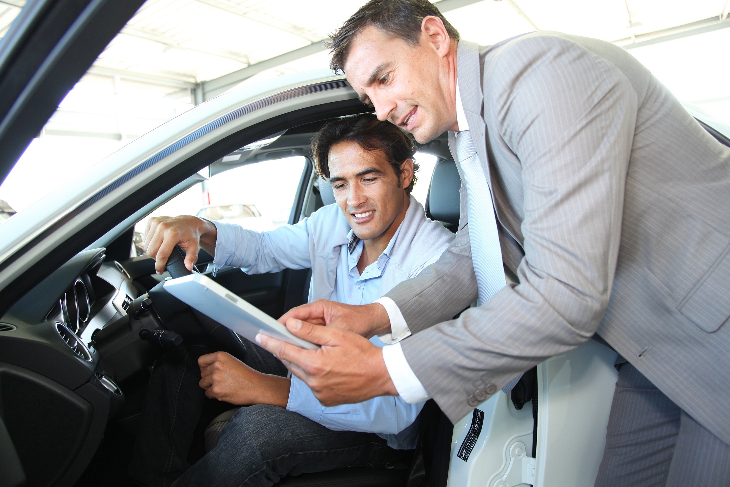 car seller with car buyer looking at electronic tablet