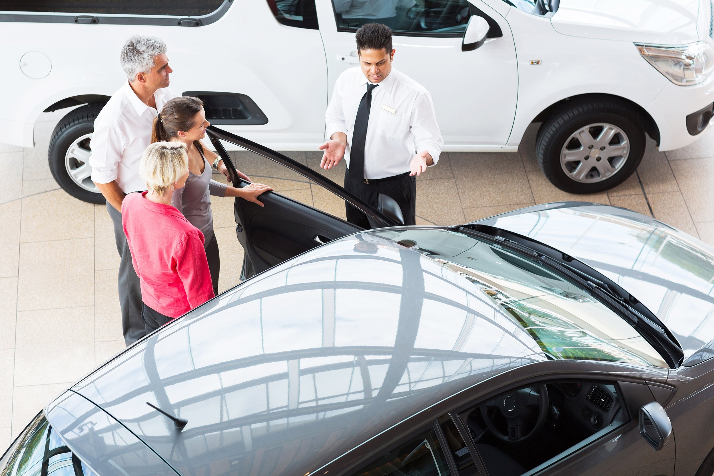 overhead view of car salesman showing new vehicle to customers