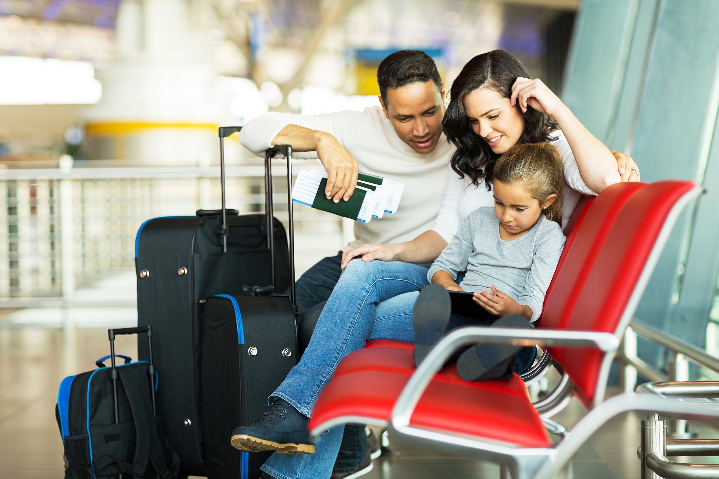 young girl with parents using tablet computer at airport while waiting for their flight