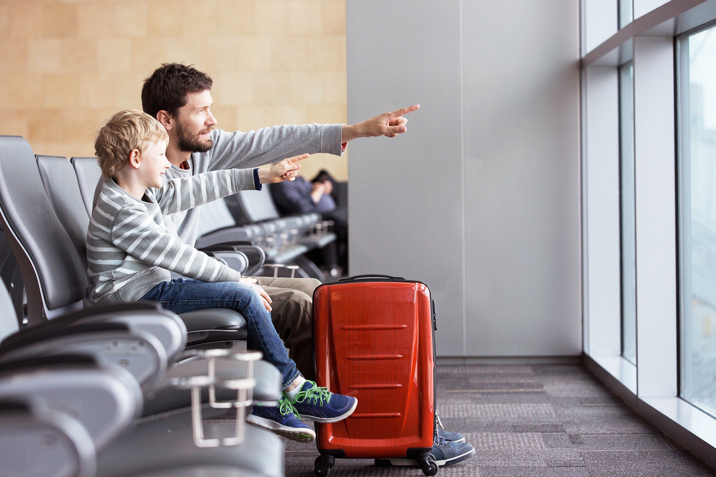 smiling boy and his father waiting at the airport for plane departure and pointing with fingers at something