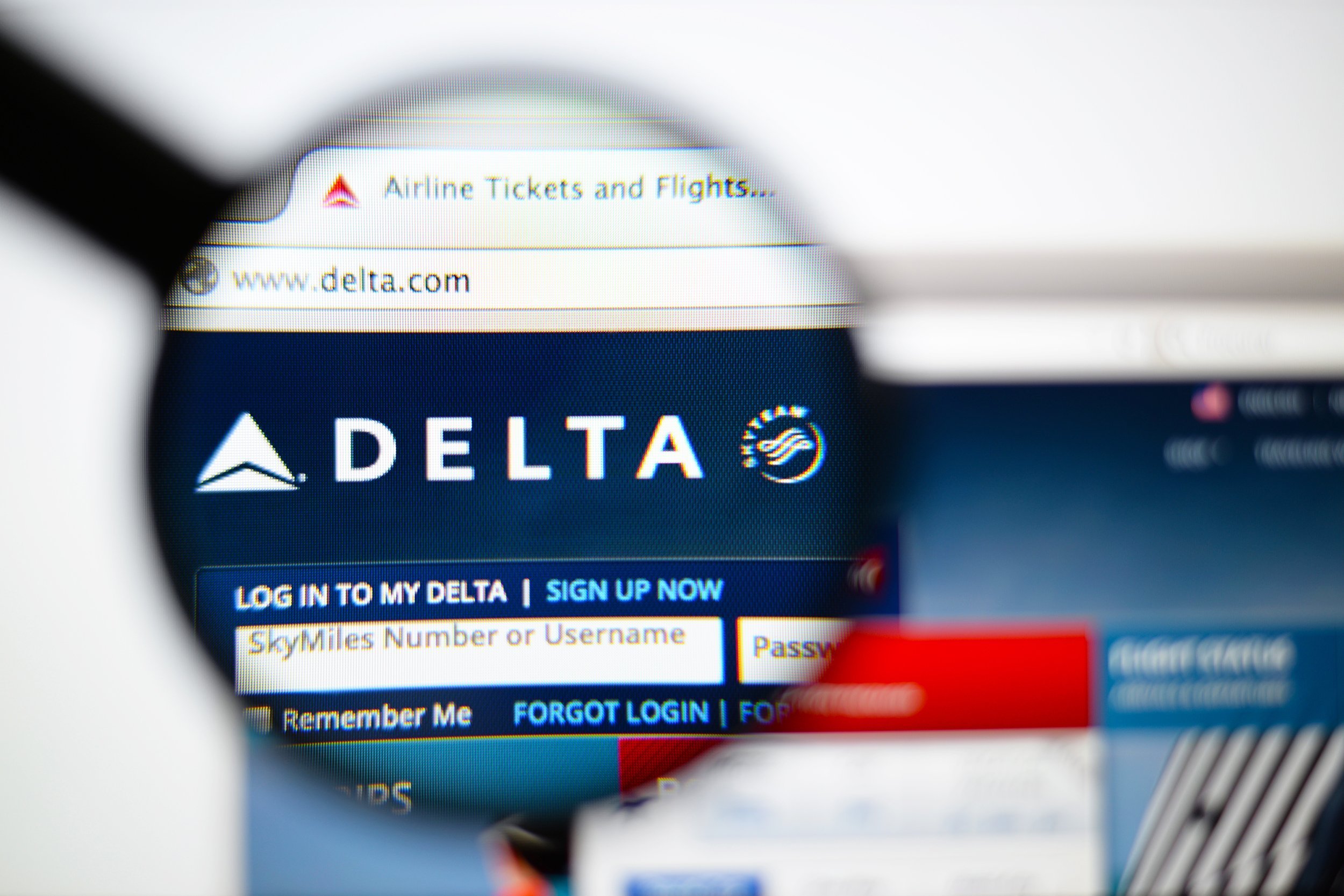 Delta Air Lines homepage on a monitor screen through a magnifying glass