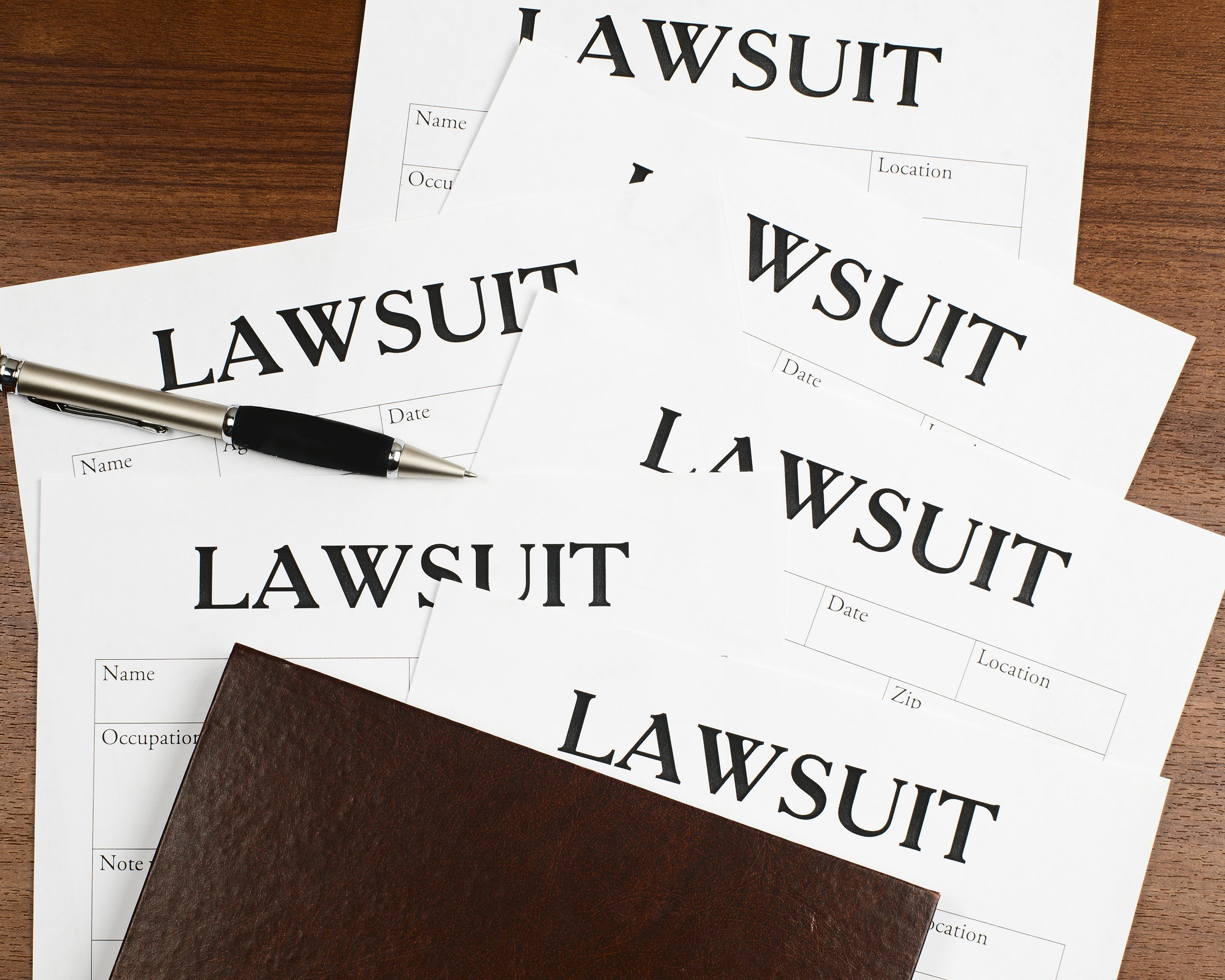 forms of the lawsuit lie on the wooden surface of the table along with a pen