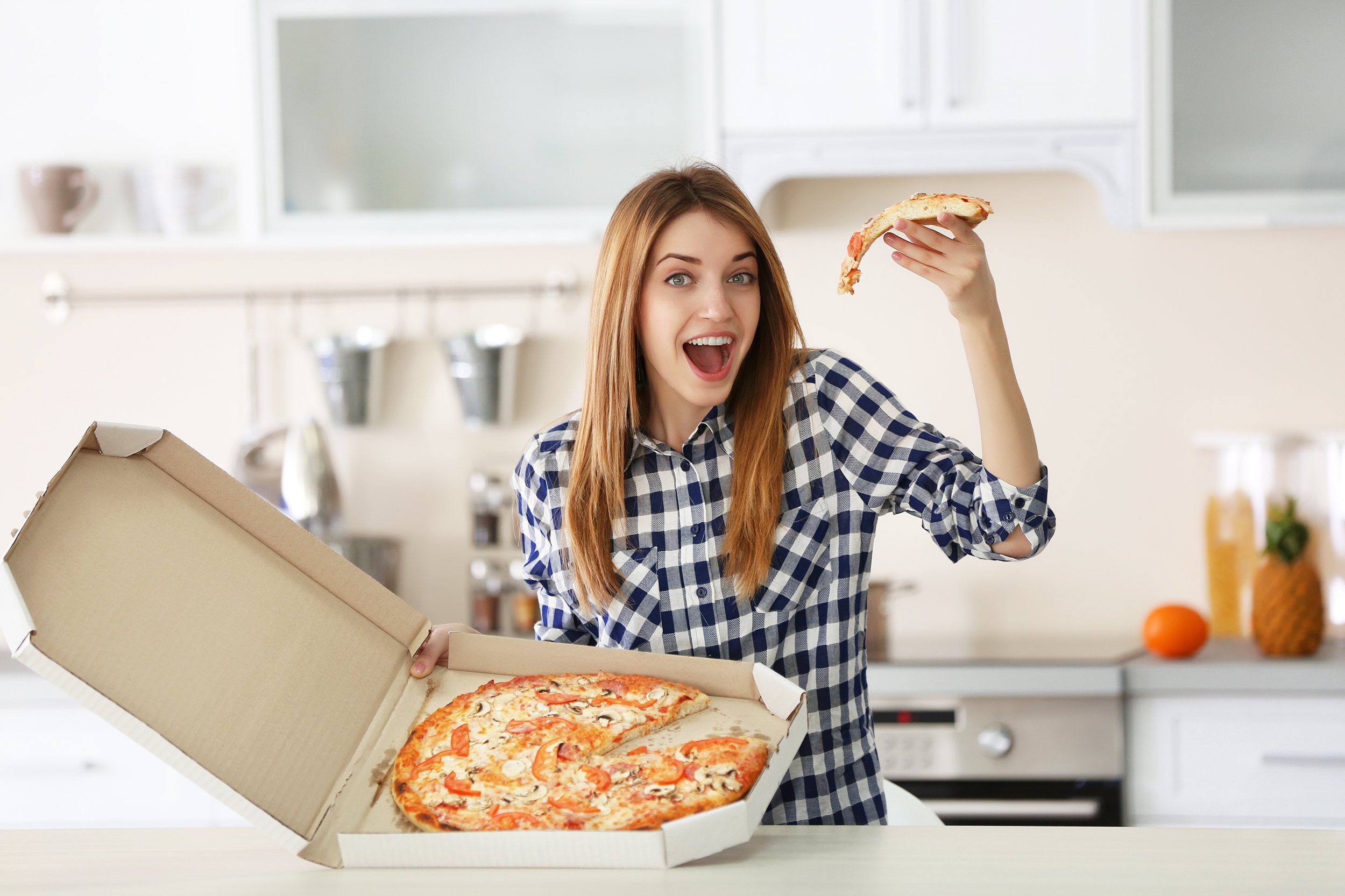 happy woman holding hot pizza in box at home