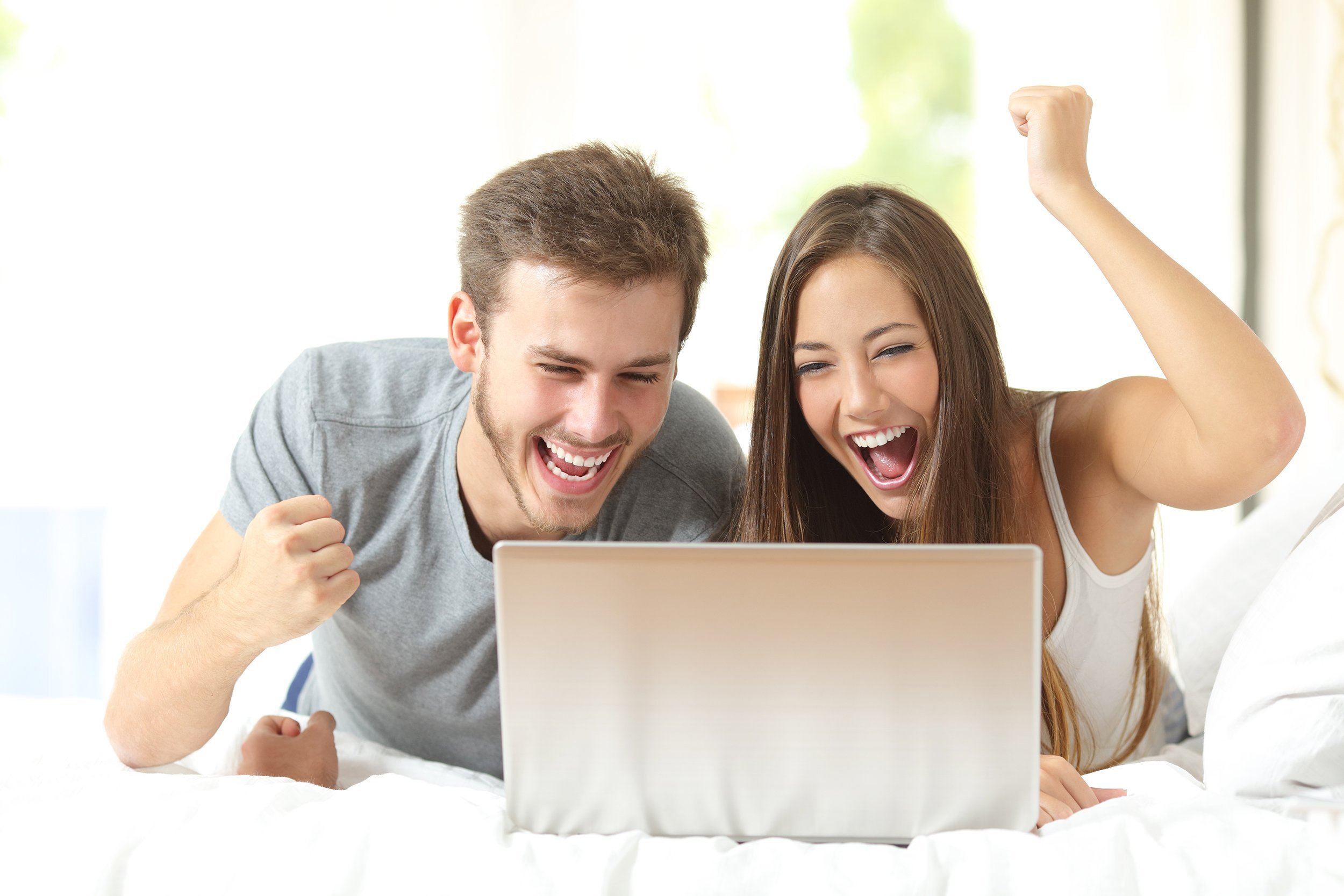 couple winning using a laptop lying on a bed at home