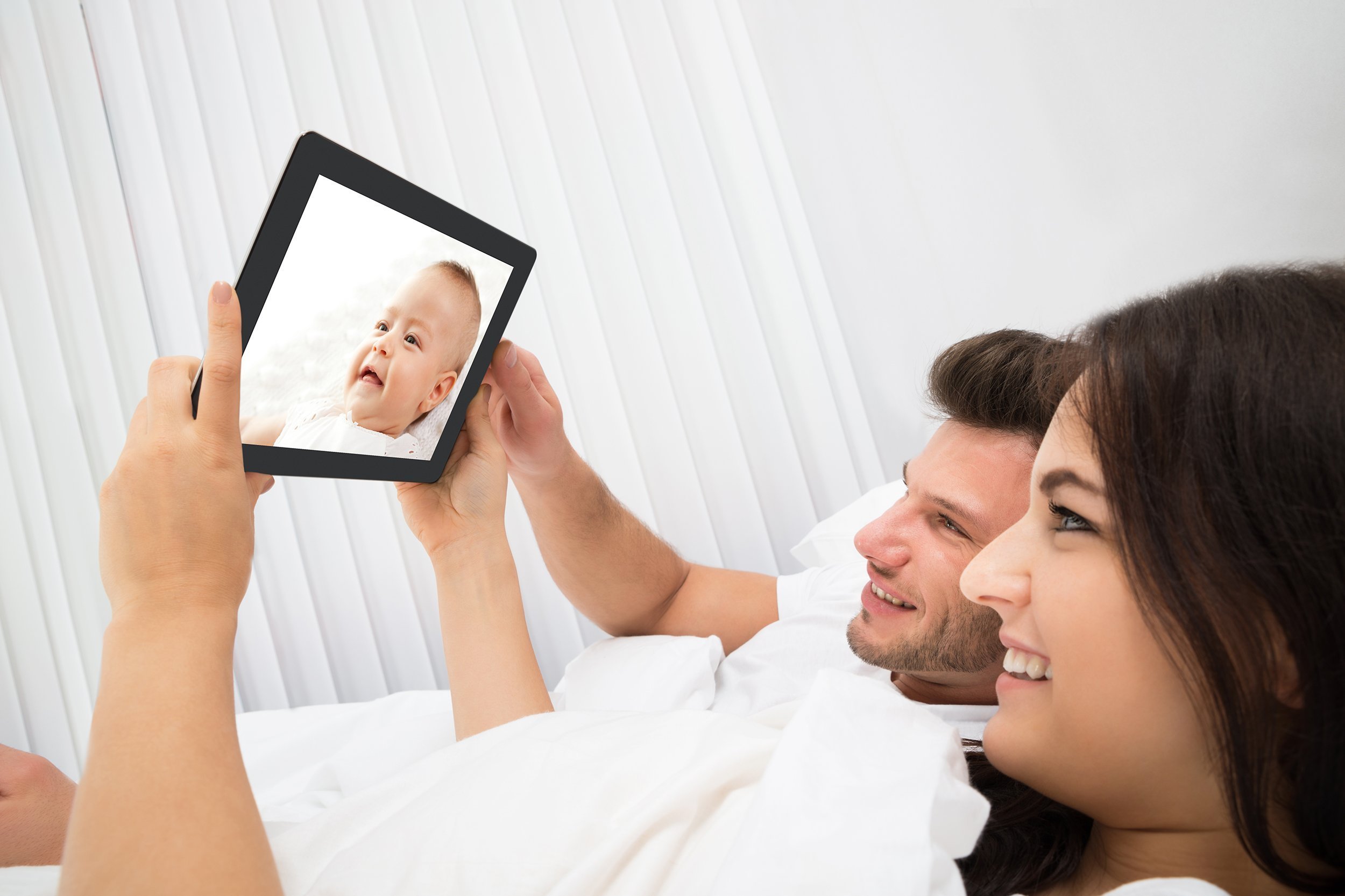 young couple on bed looking at baby on digital tablet