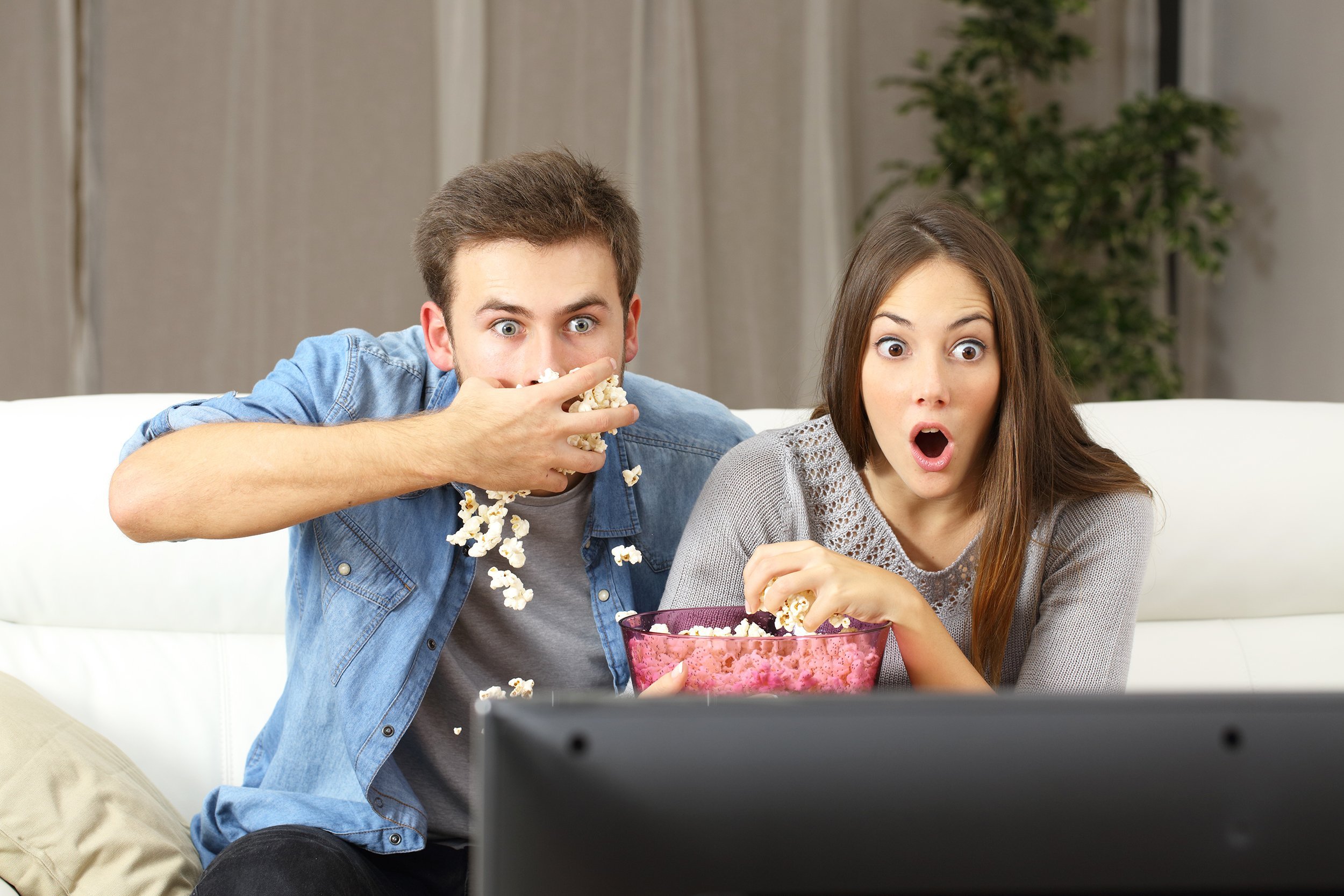 amazed couple watching tv program sitting on a couch at home