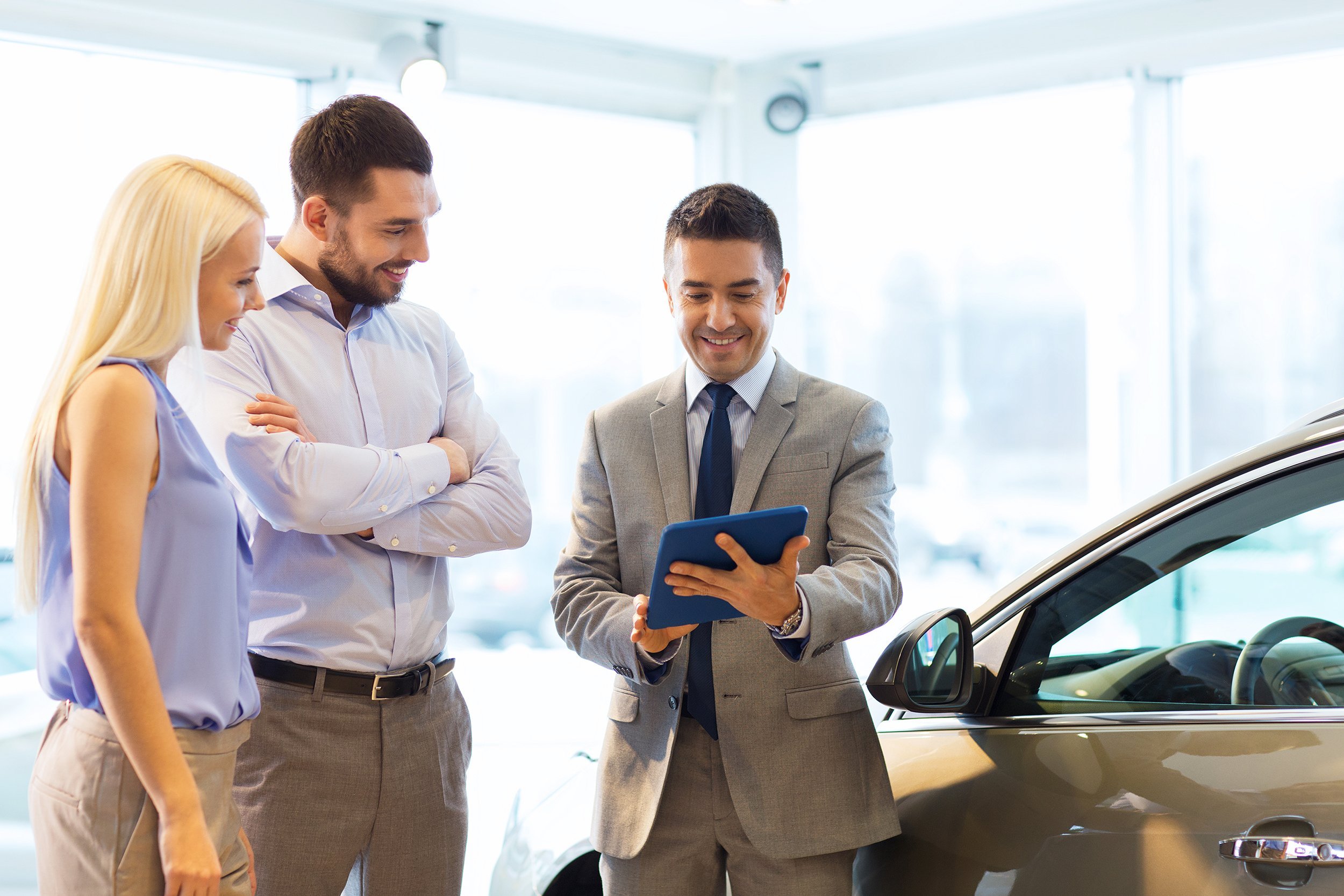 happy couple with car dealer in auto show room