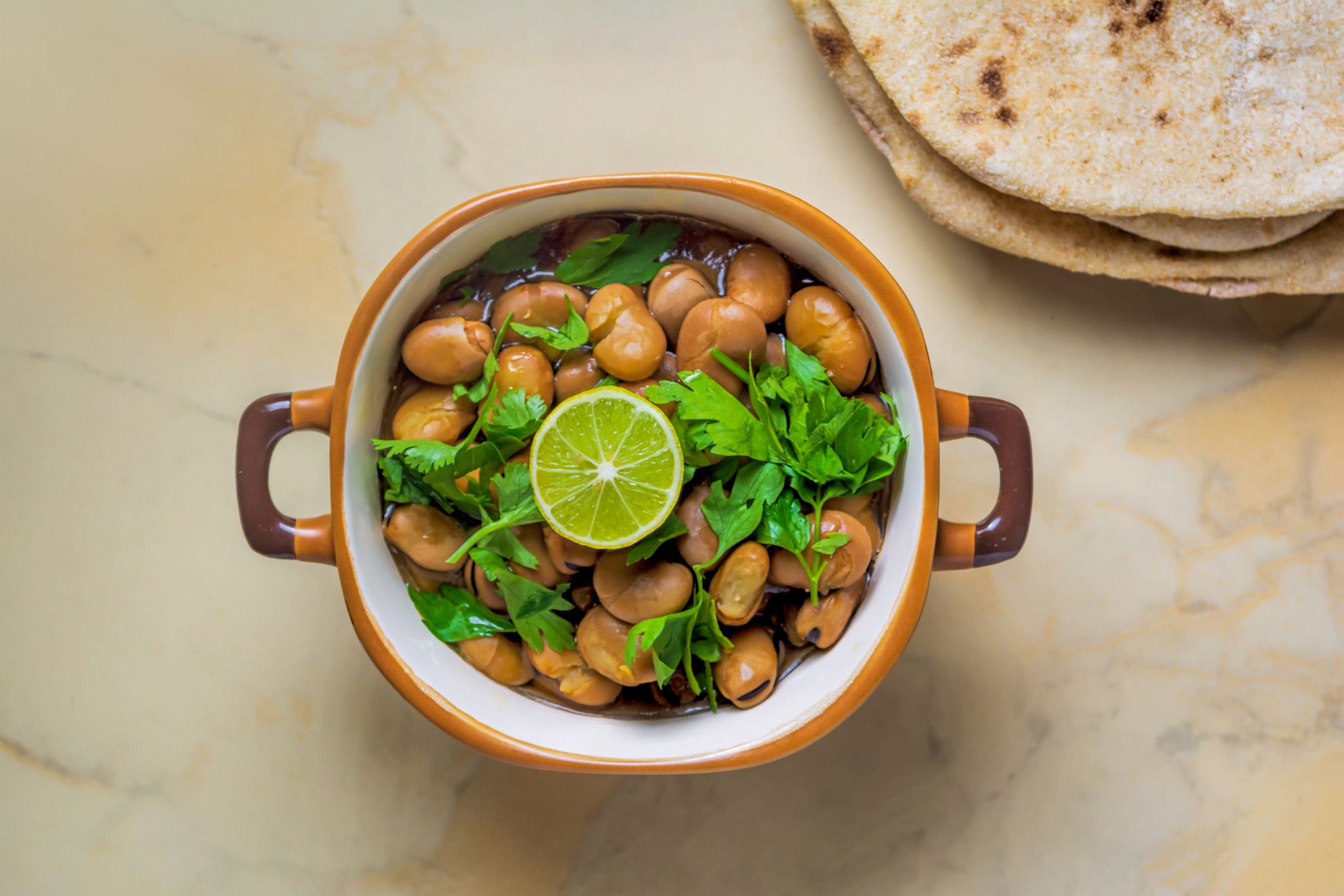 Ful Medames - Dish of Egyptian fava beans with lemon ,cumin ,vegetable oil and chopped parsley, served with flat bread on a marble background, popular vegan dish throughout the Middle East