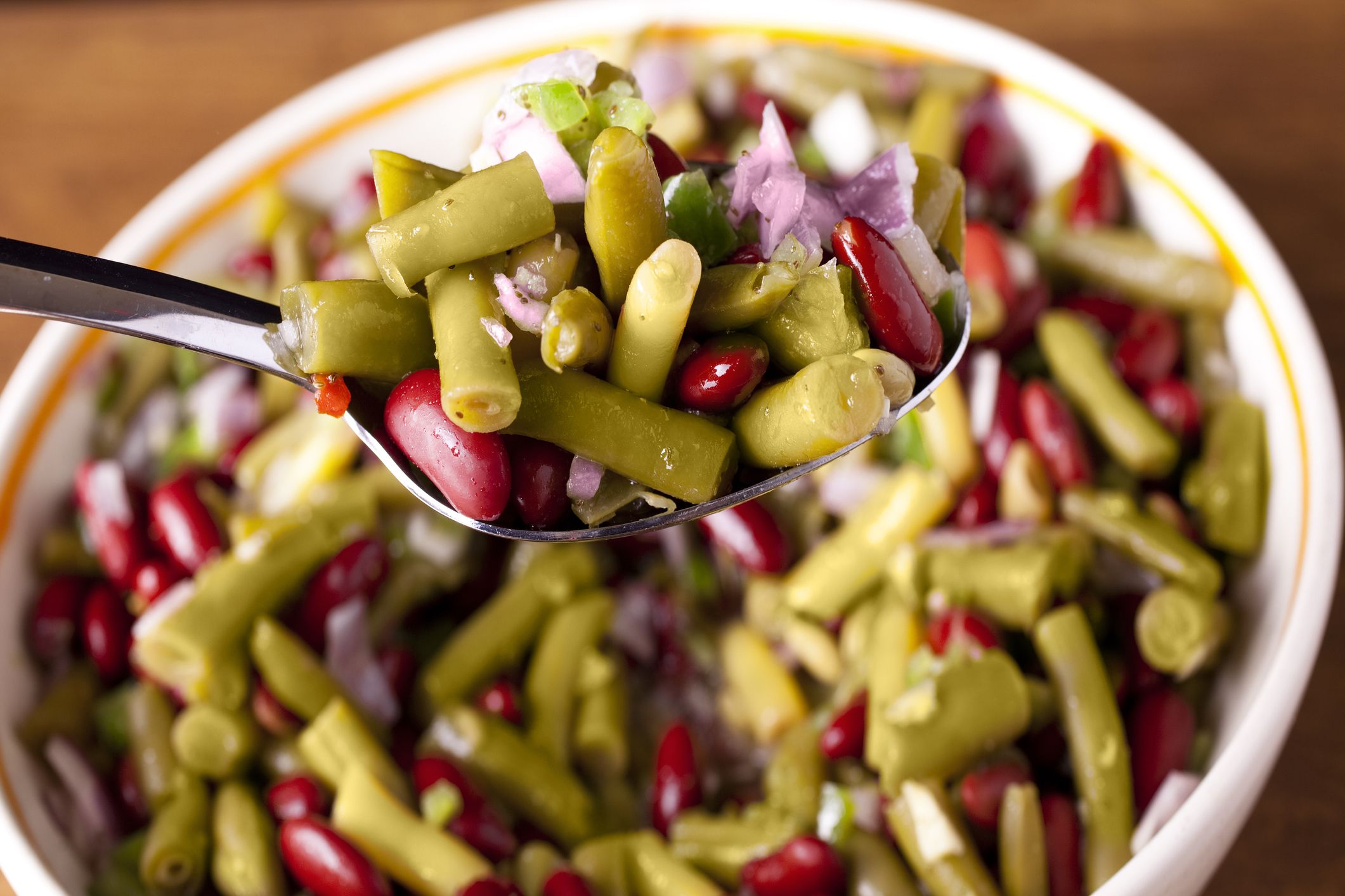 Bowl of three bean salad with ingredients. Green beans, kidney beans, onions, garlic, bell pepper. Close-up. Spoon in serving bowl.