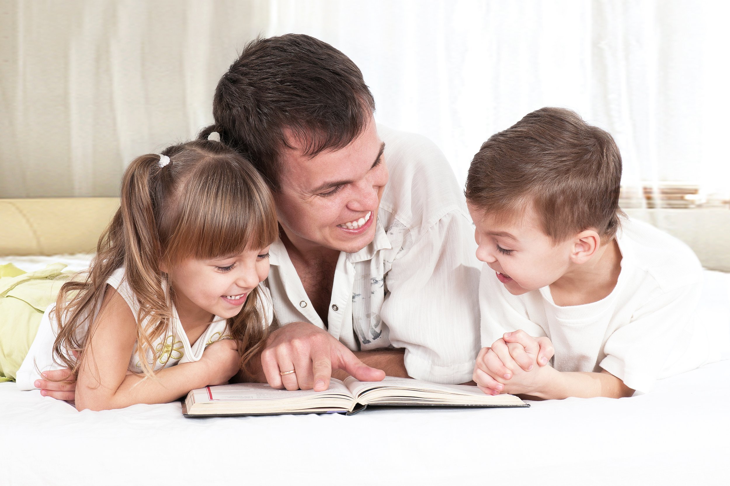 father with children, reading a book, on the bed