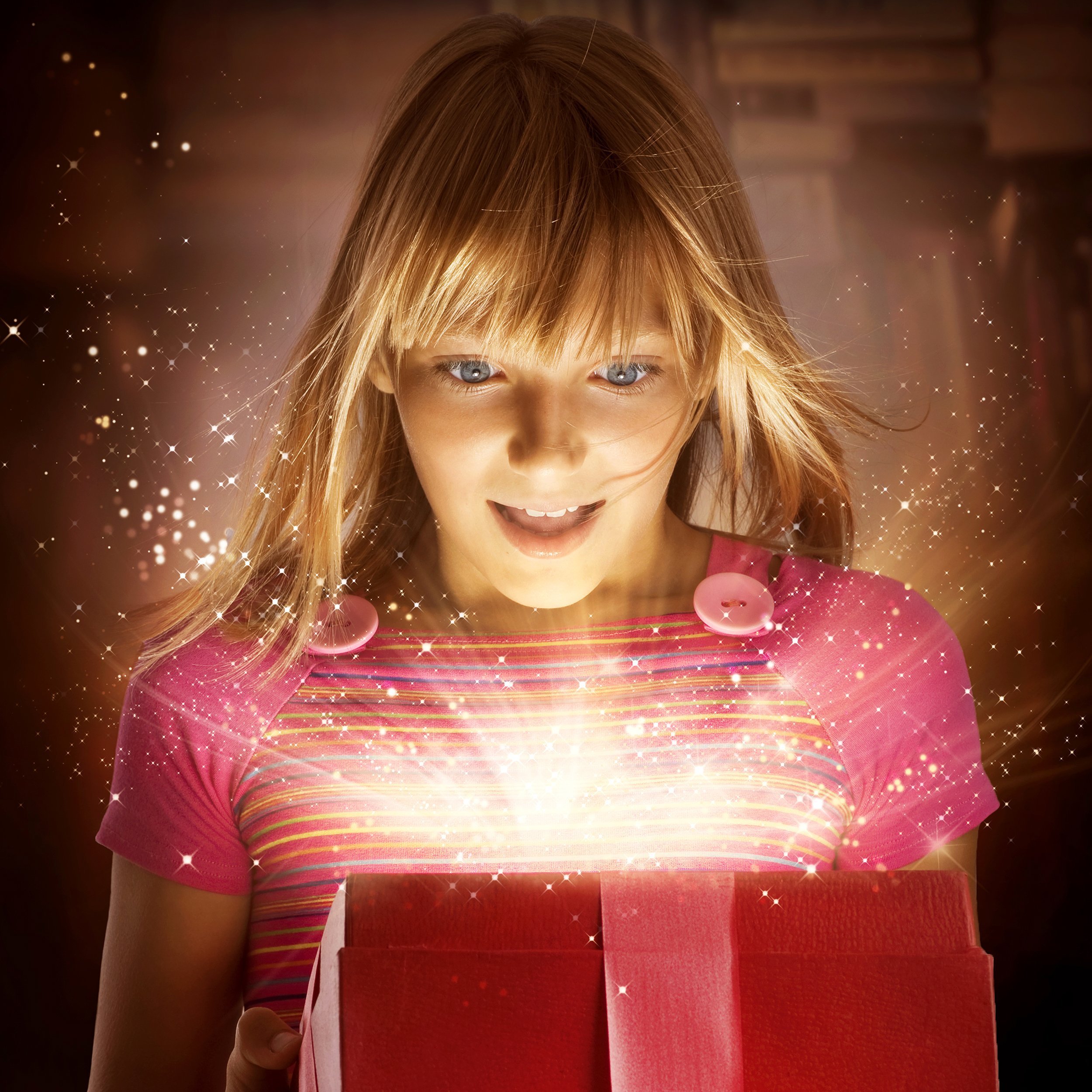 happy child looking inside red gift box with sparkles coming out of it