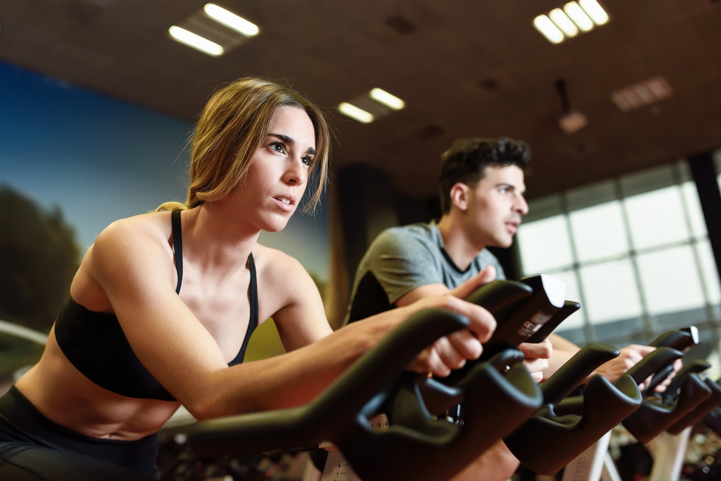woman and man biking in the gym doing cardio workout on cycling bikes