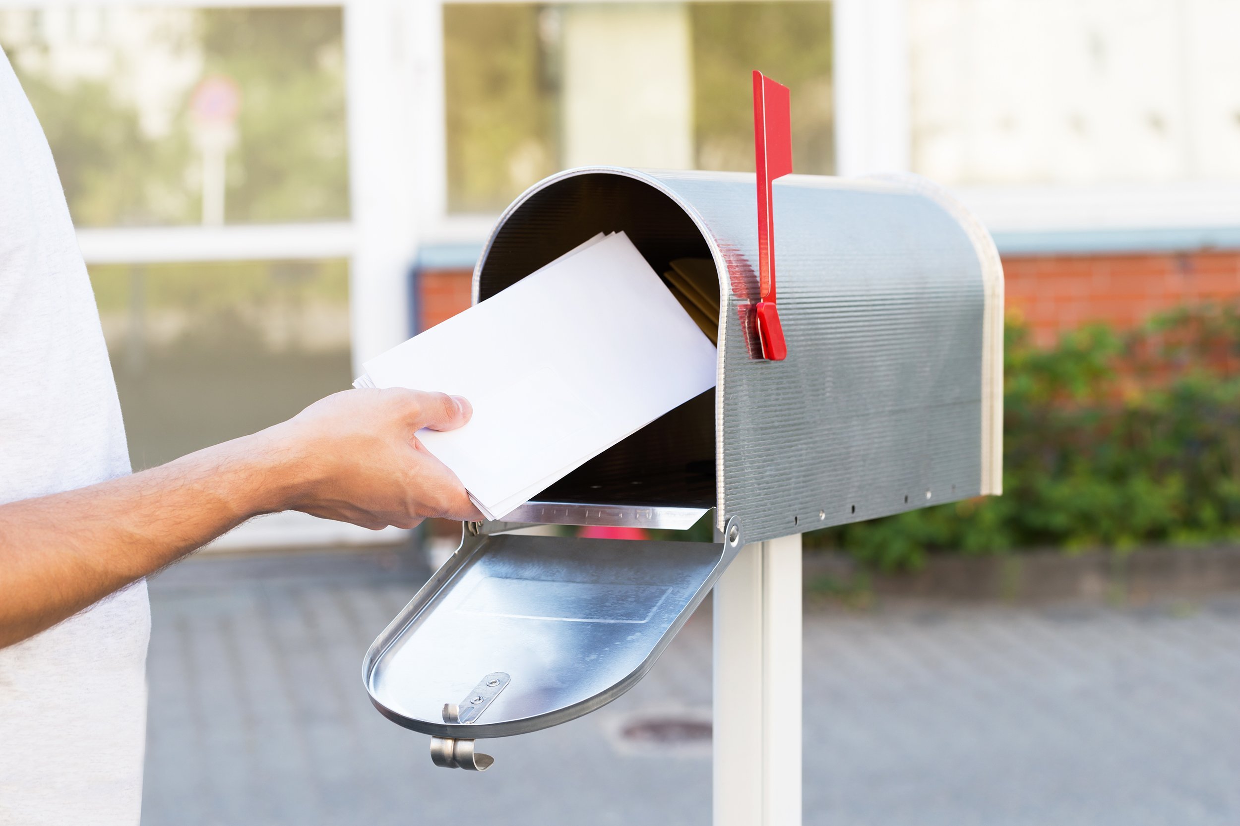 close-up of person putting stack of letters in mailbox