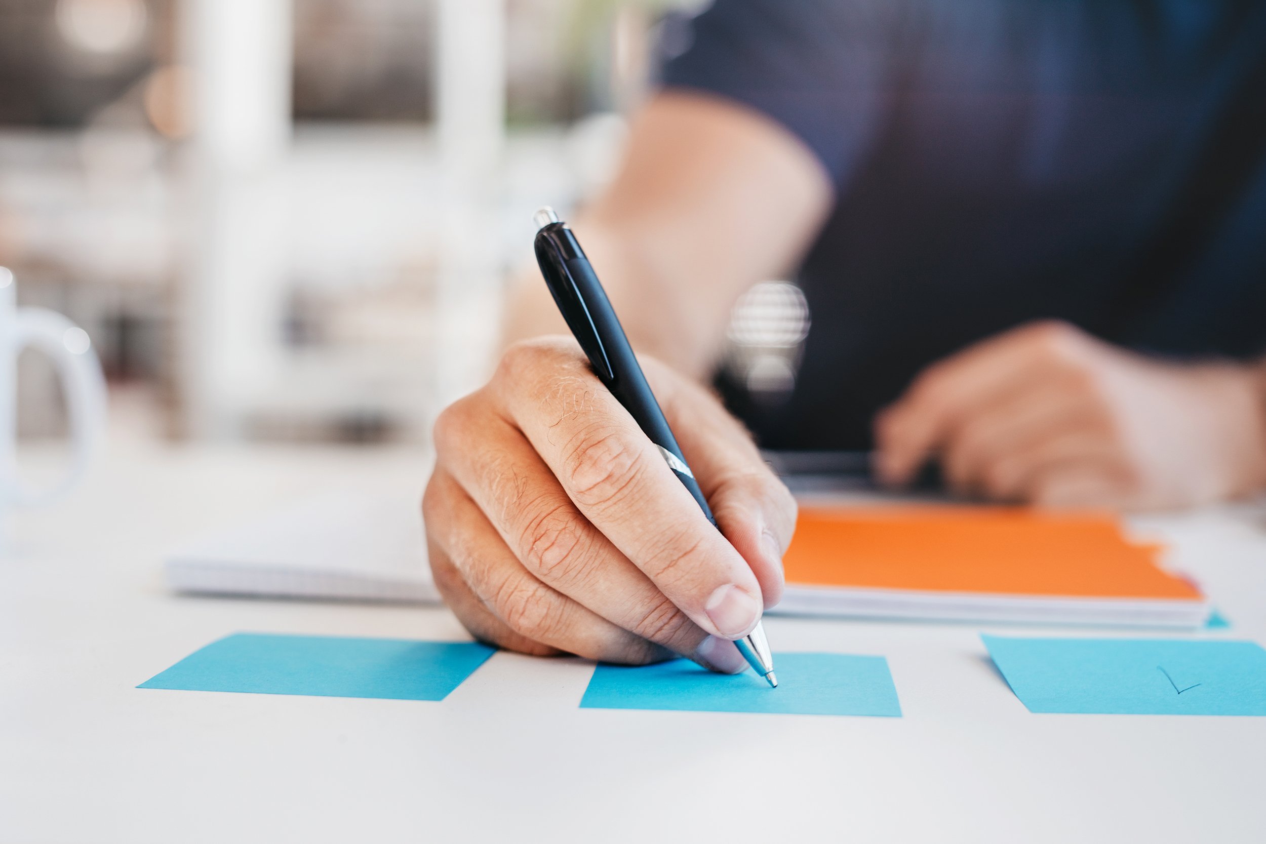 close up image of business man writing on an adhesive note at table in office