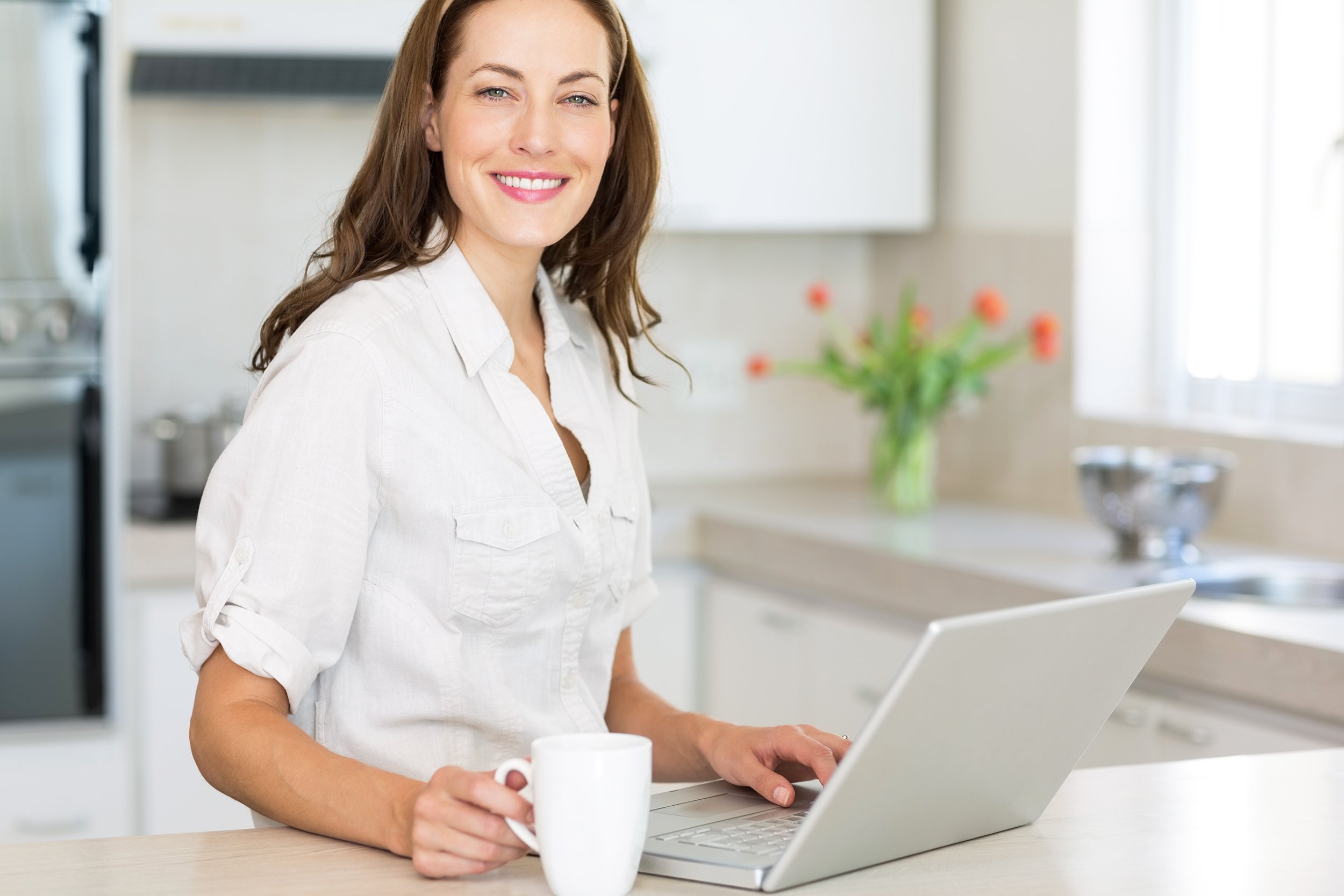 smiling young woman using laptop in the kitchen at home
