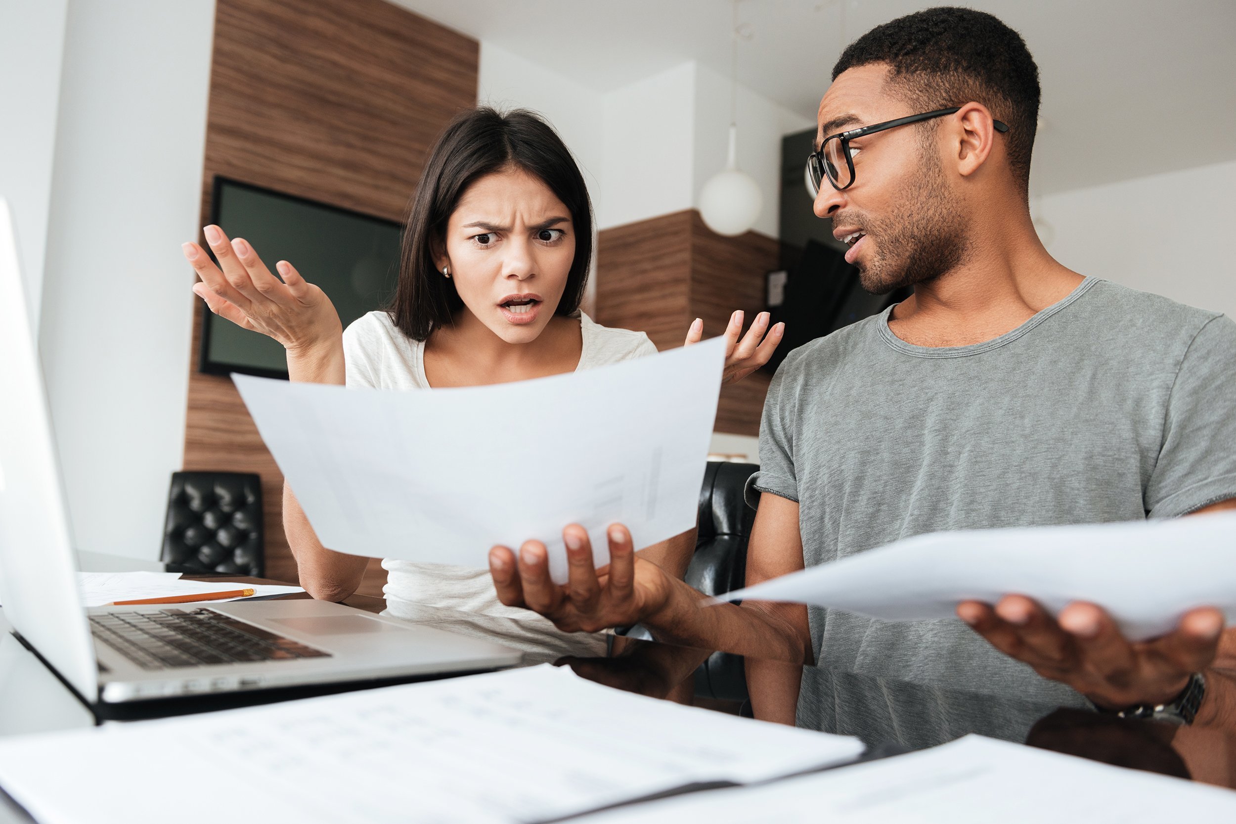 frustrated young couple discussing about domestic bills at home while looking at documents