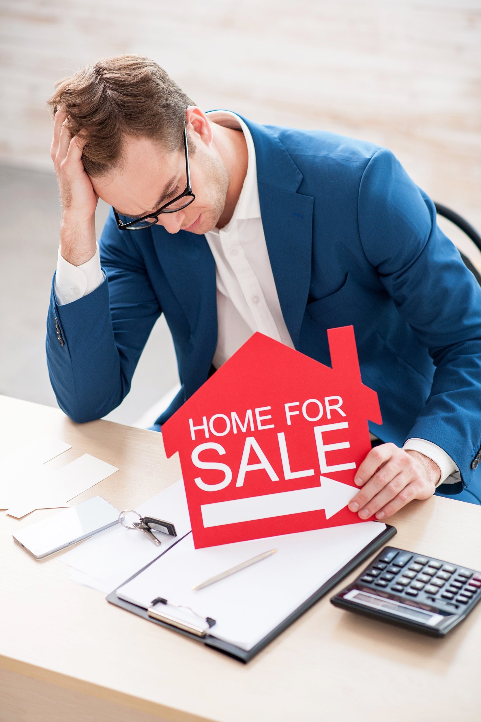 sad young realtor is sitting at the desk and looking down with frustration