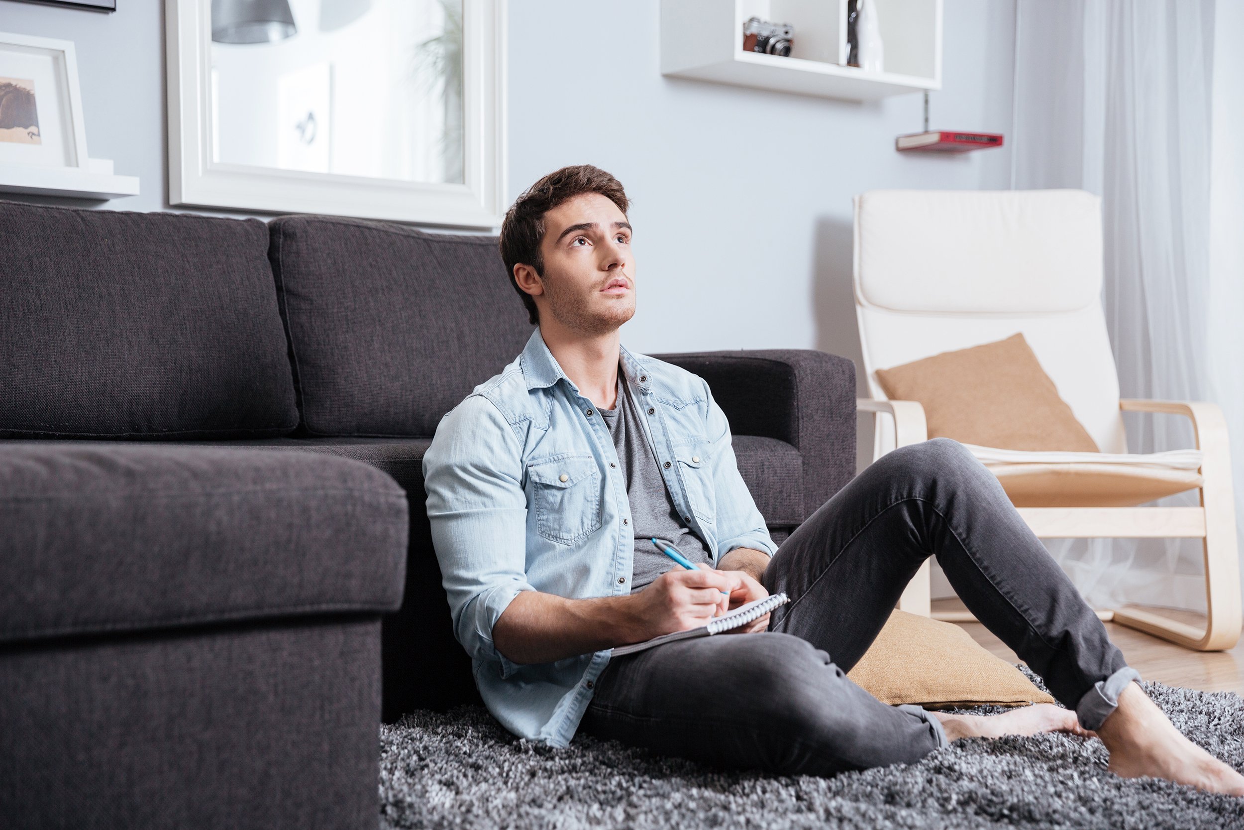 young casual man thinking about something and making notes in copybook at home