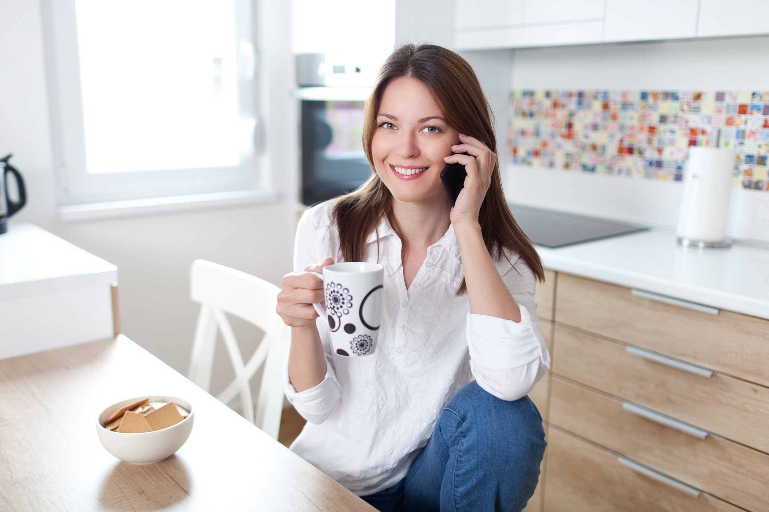 young woman using cell phone and having a coffee in the kitchen