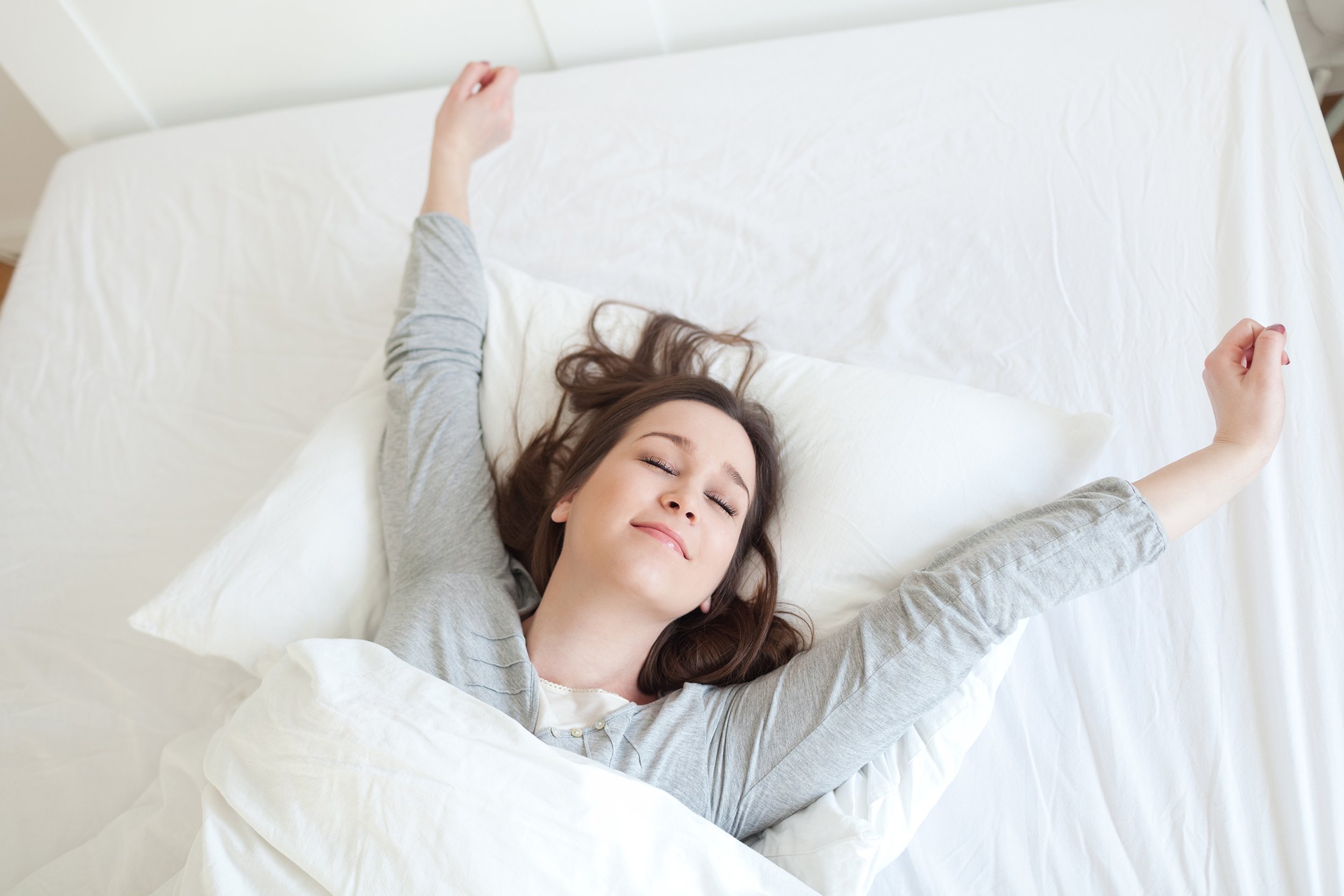 woman waking up in bed stretching her arms