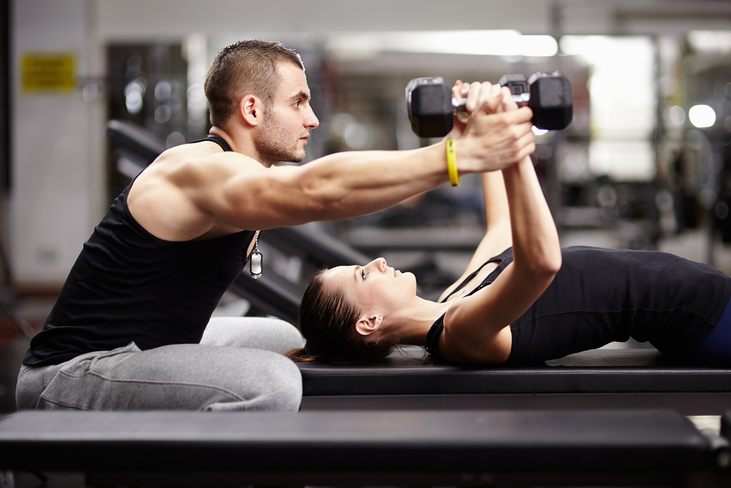 personal trainer helping woman working with heavy dumbbells