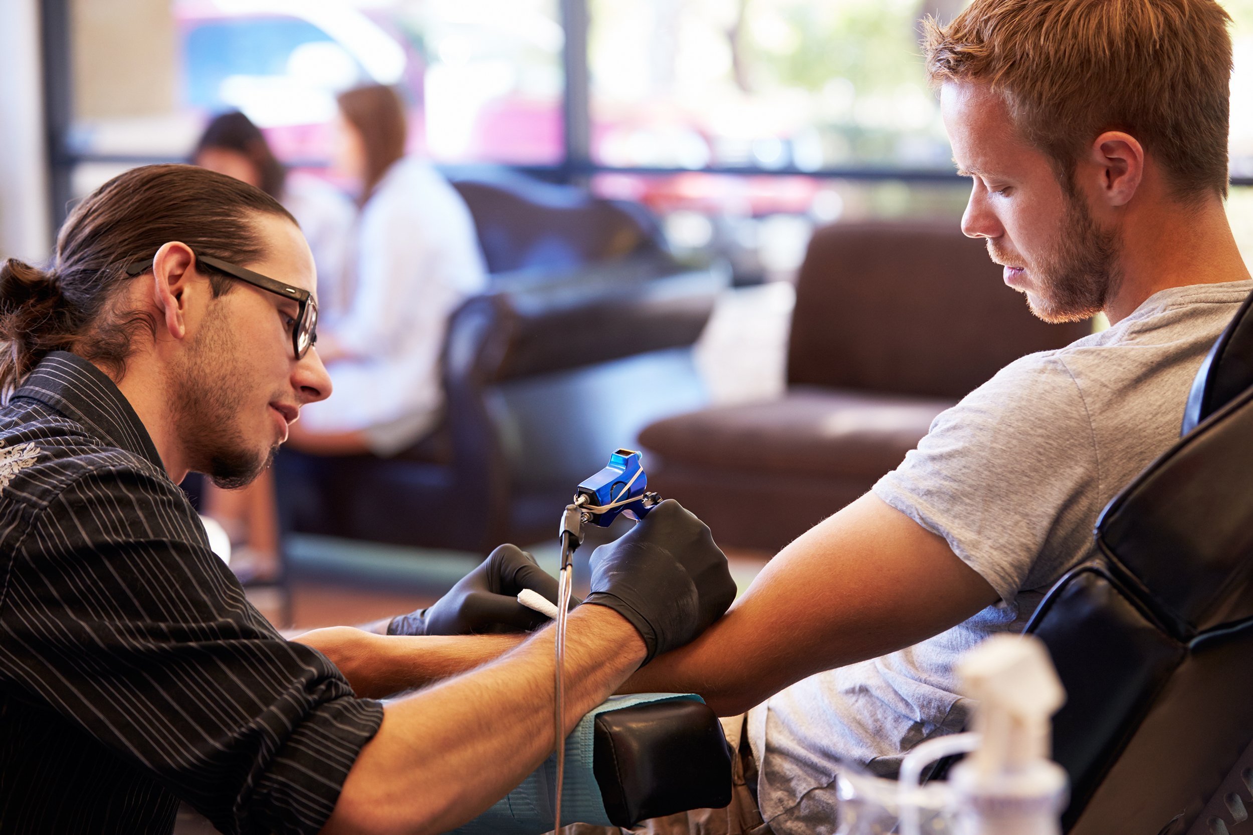 man sitting in chair having tattoo on arm in parlor