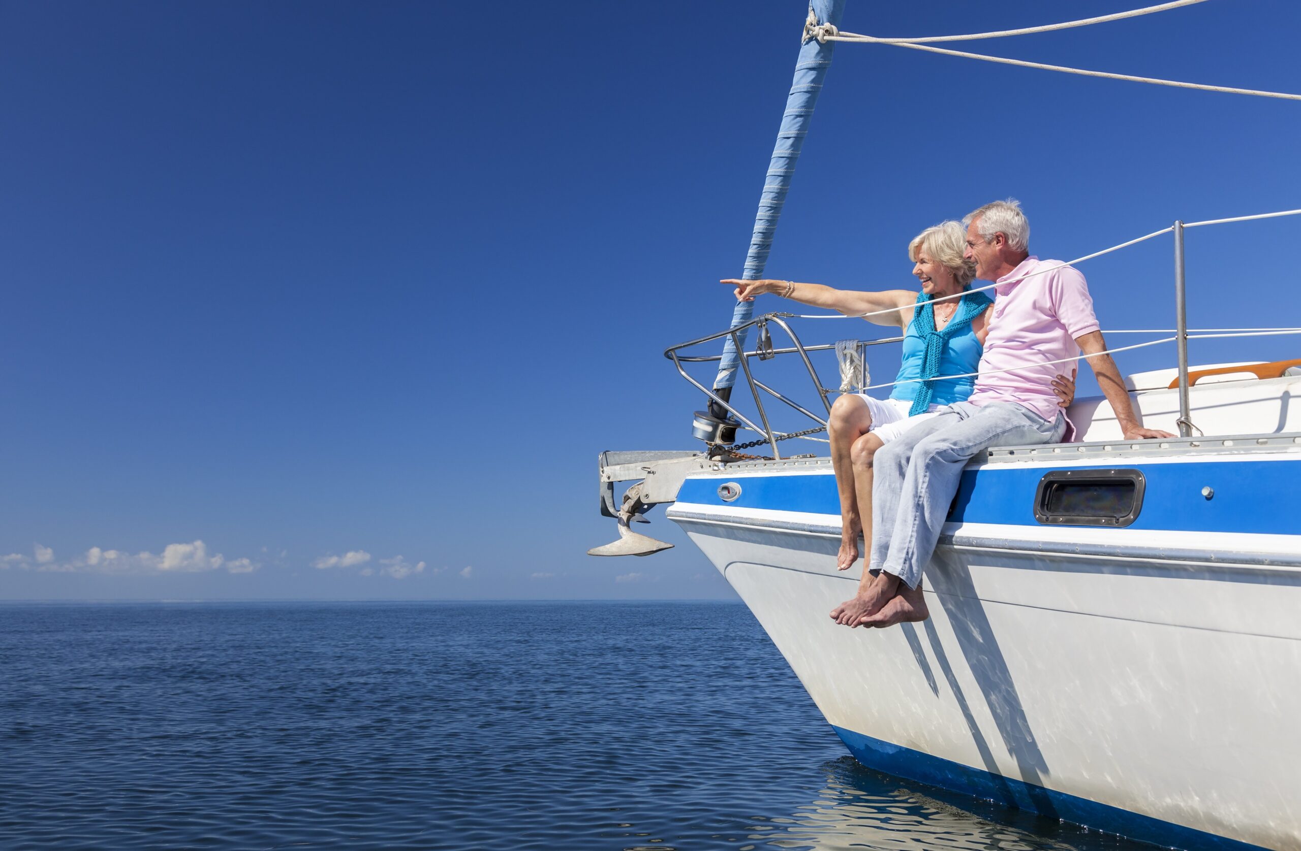 A happy older couple sits on the bow of a yacht viewing something in the distance