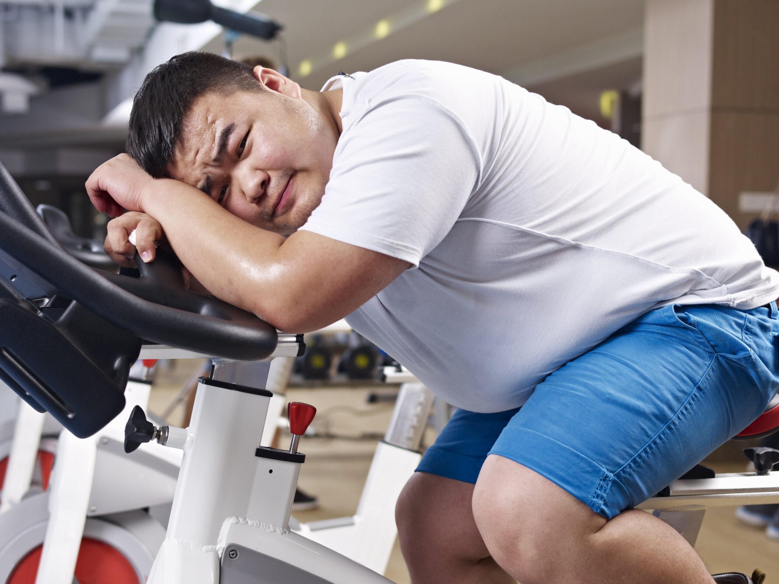 overweight man at gym exhausted and leaning on exercise cycle