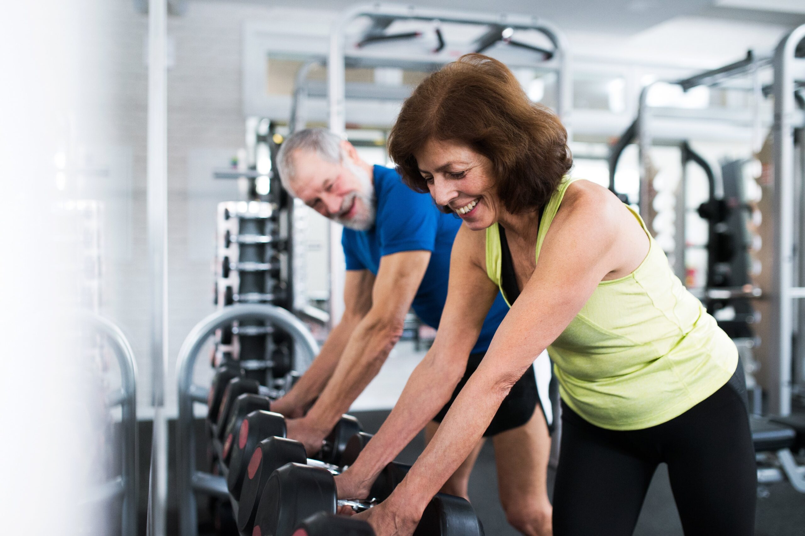 senior couple in the gym reaching for dumbbell weights