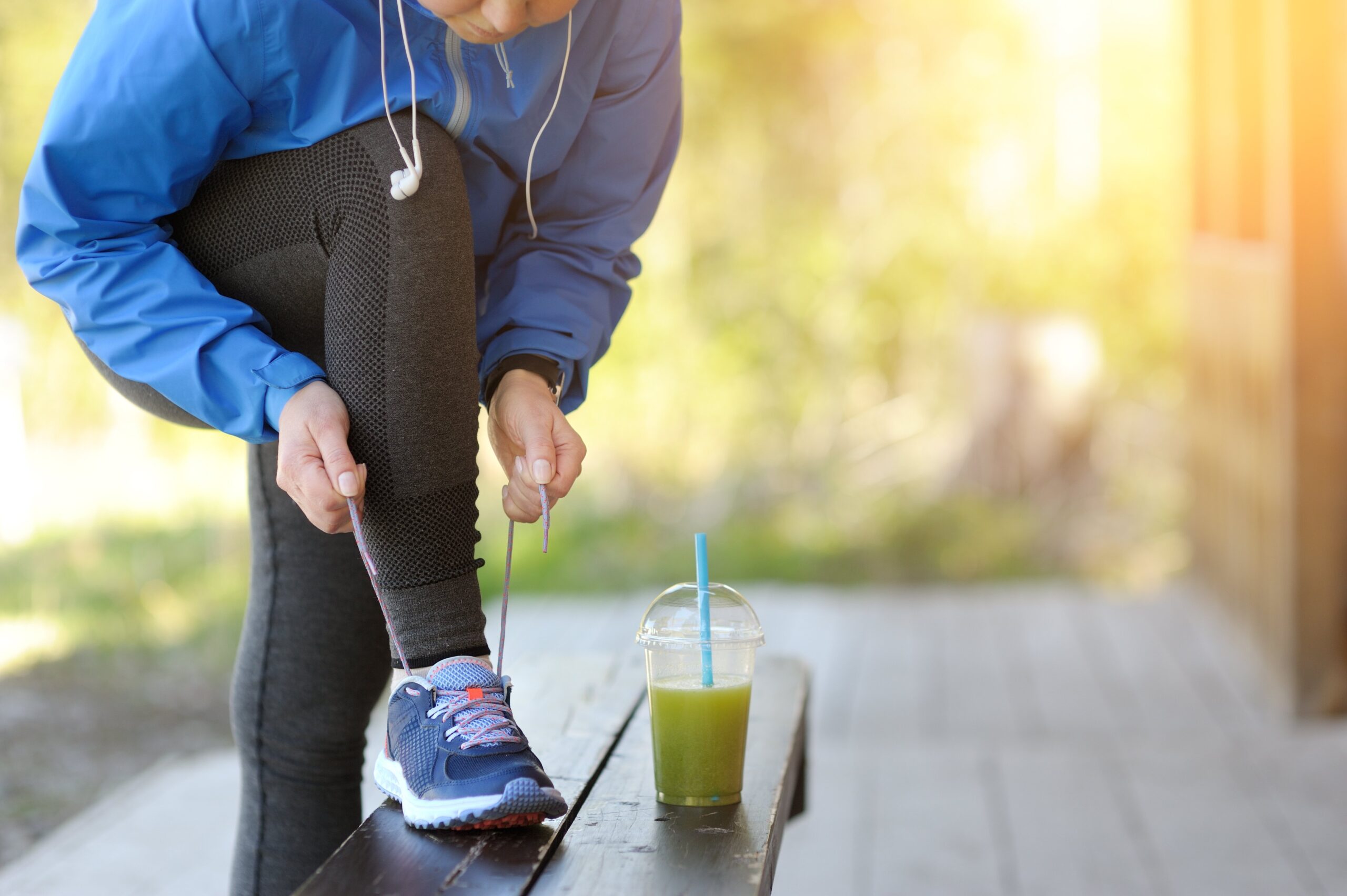 a woman laces up her running shoes with a green smoothie sitting in front of her