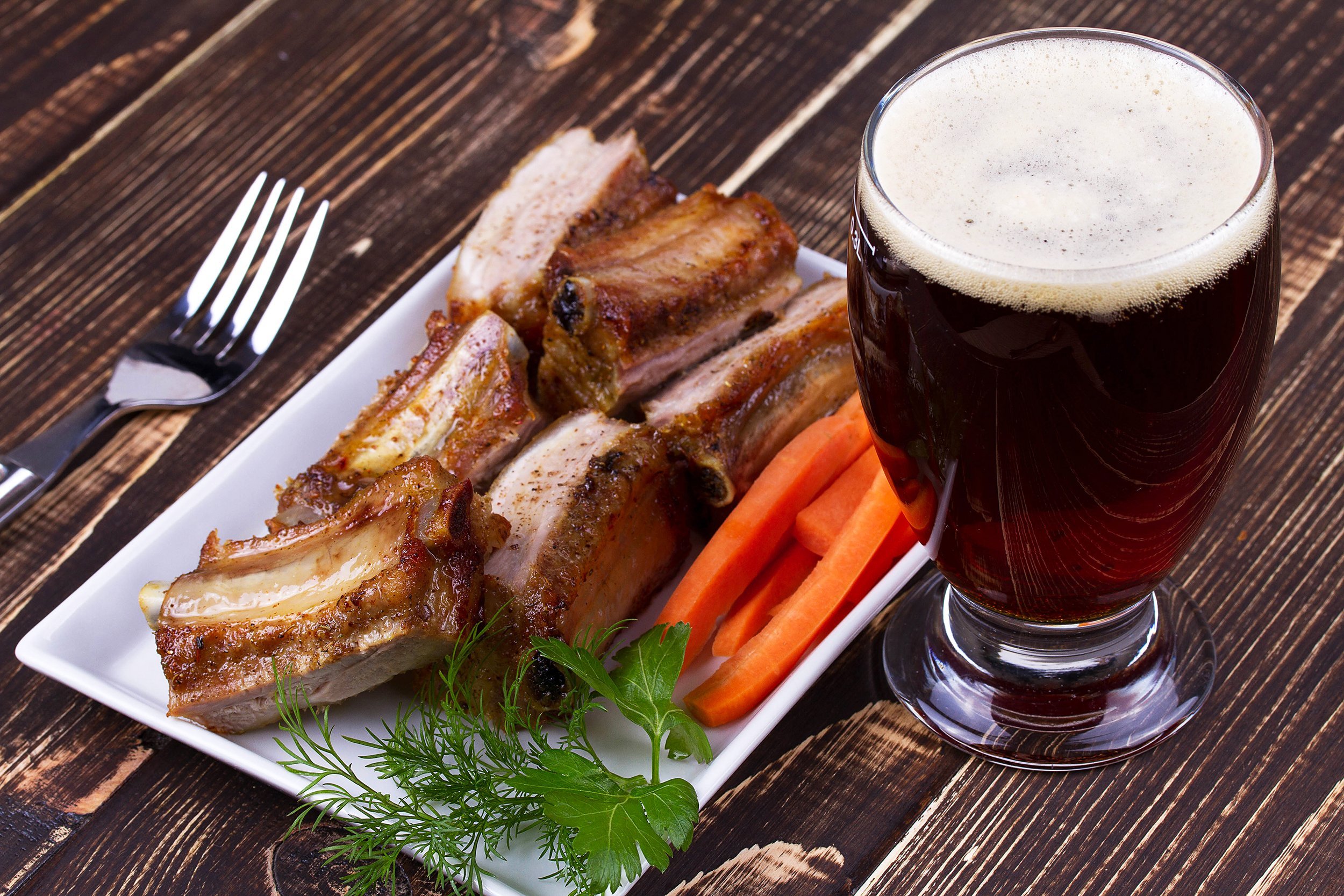 glass of beer and pork ribs with carrot on wooden table