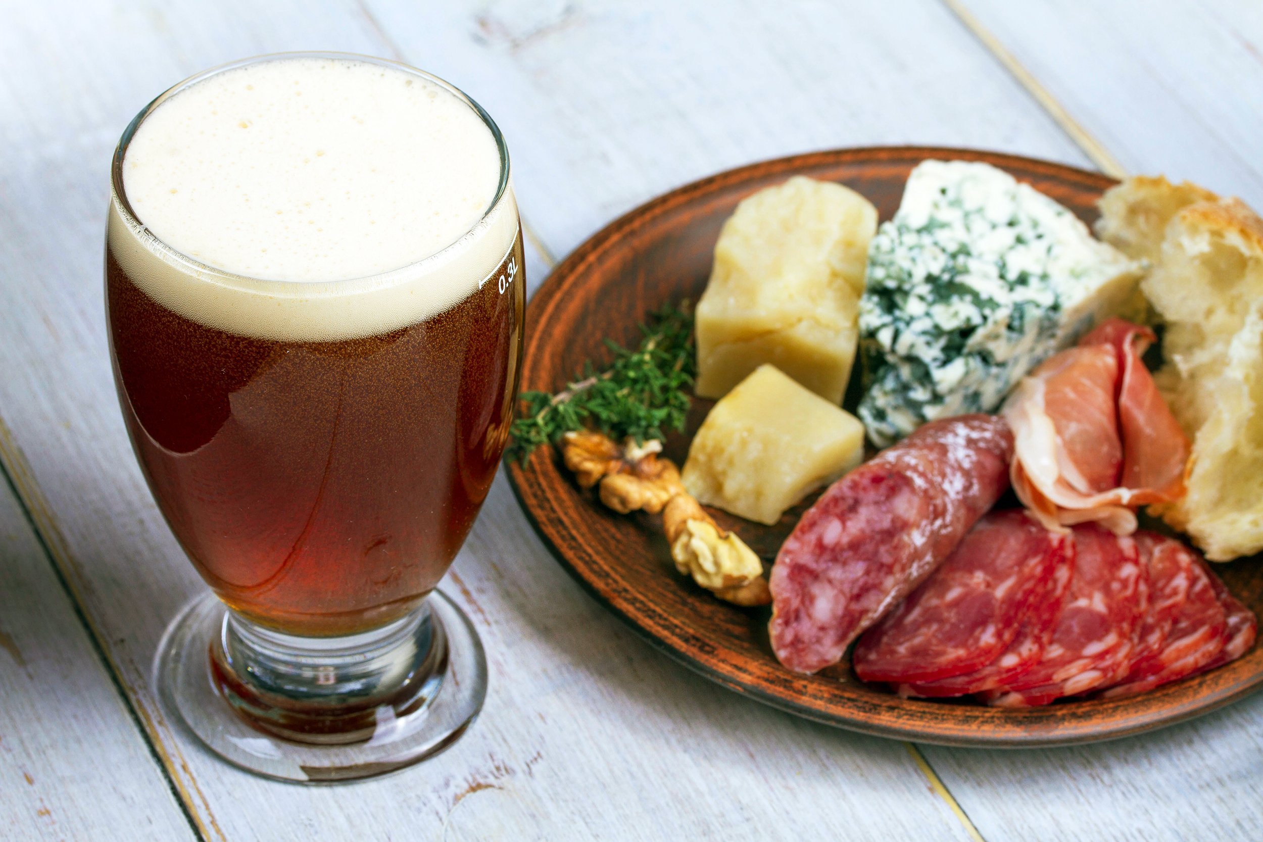 glass of beer with cheese, prosciutto, salami, rosemary, nuts, olives and bread