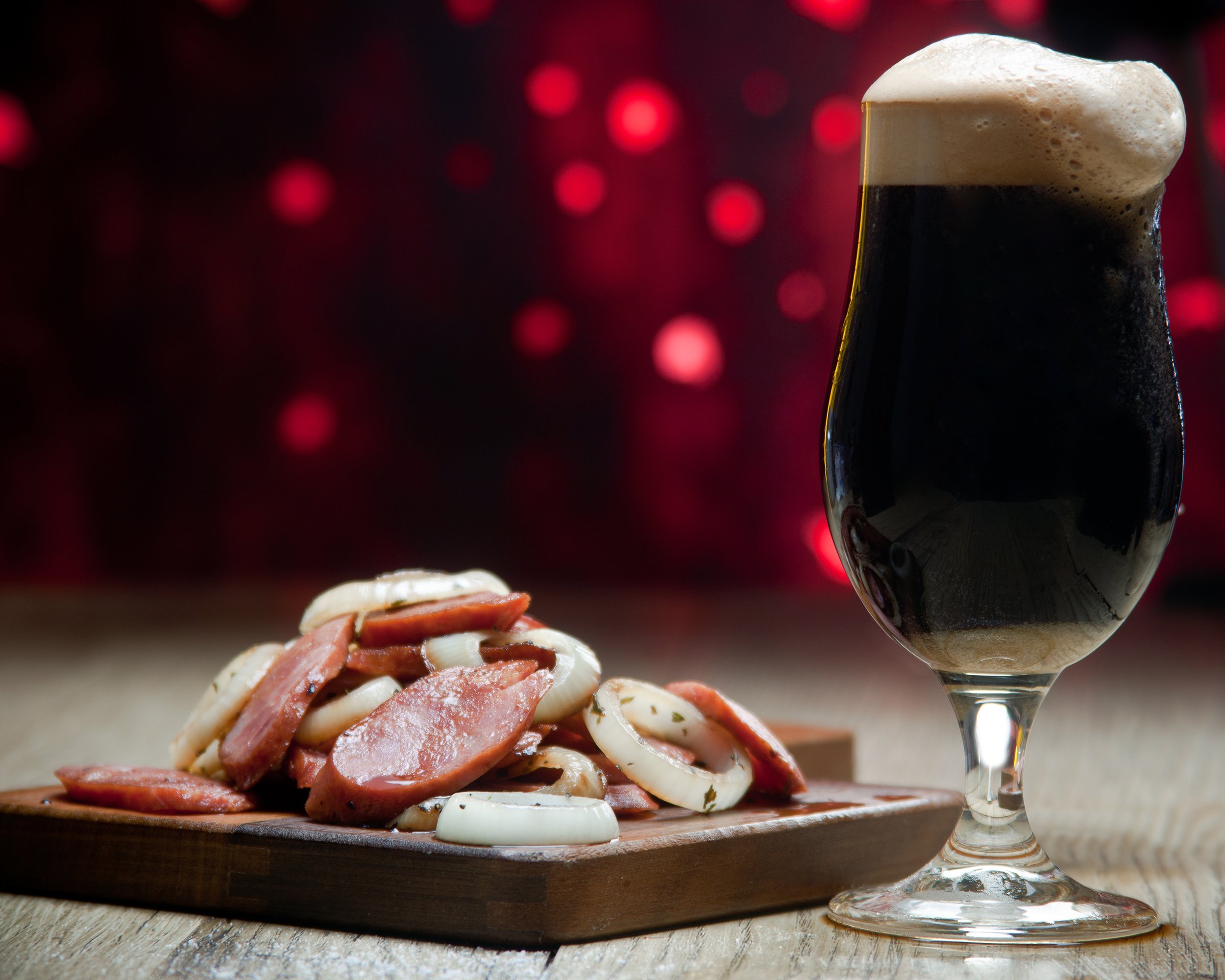 glass of dark beer, sausages and sliced onion