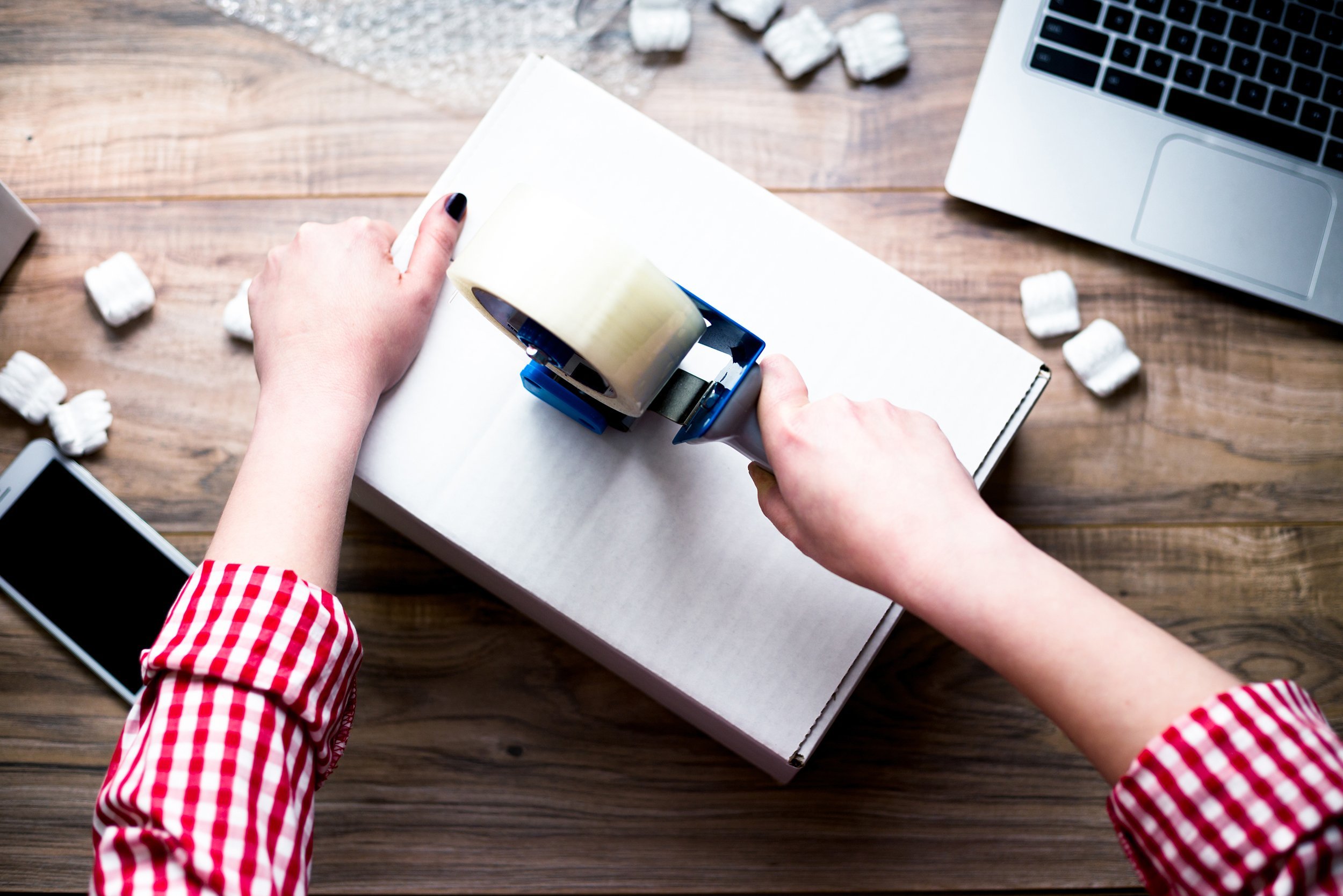 woman sealing a box with tape on desk with laptop