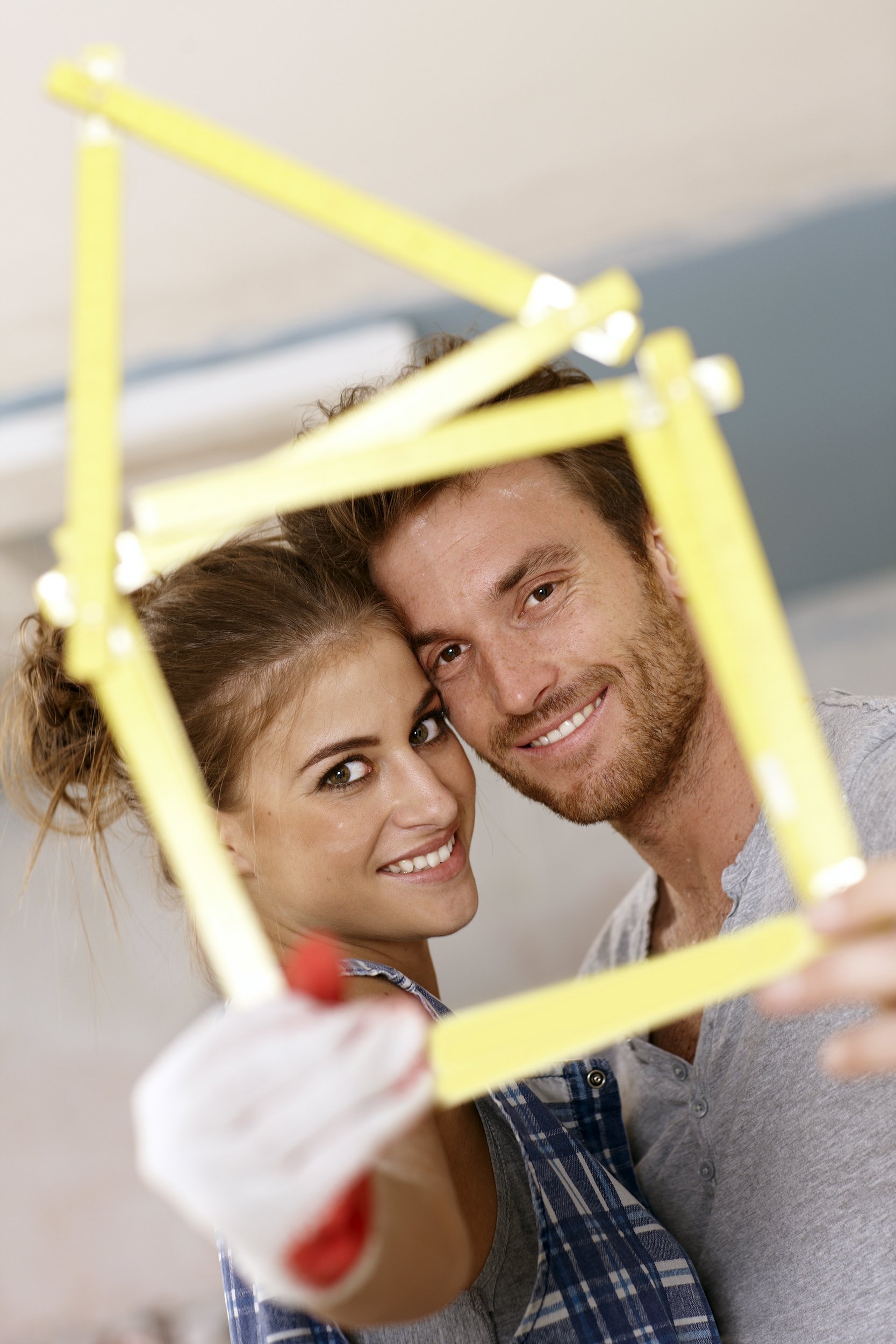 happy young couple smiling through little house formed by ruler