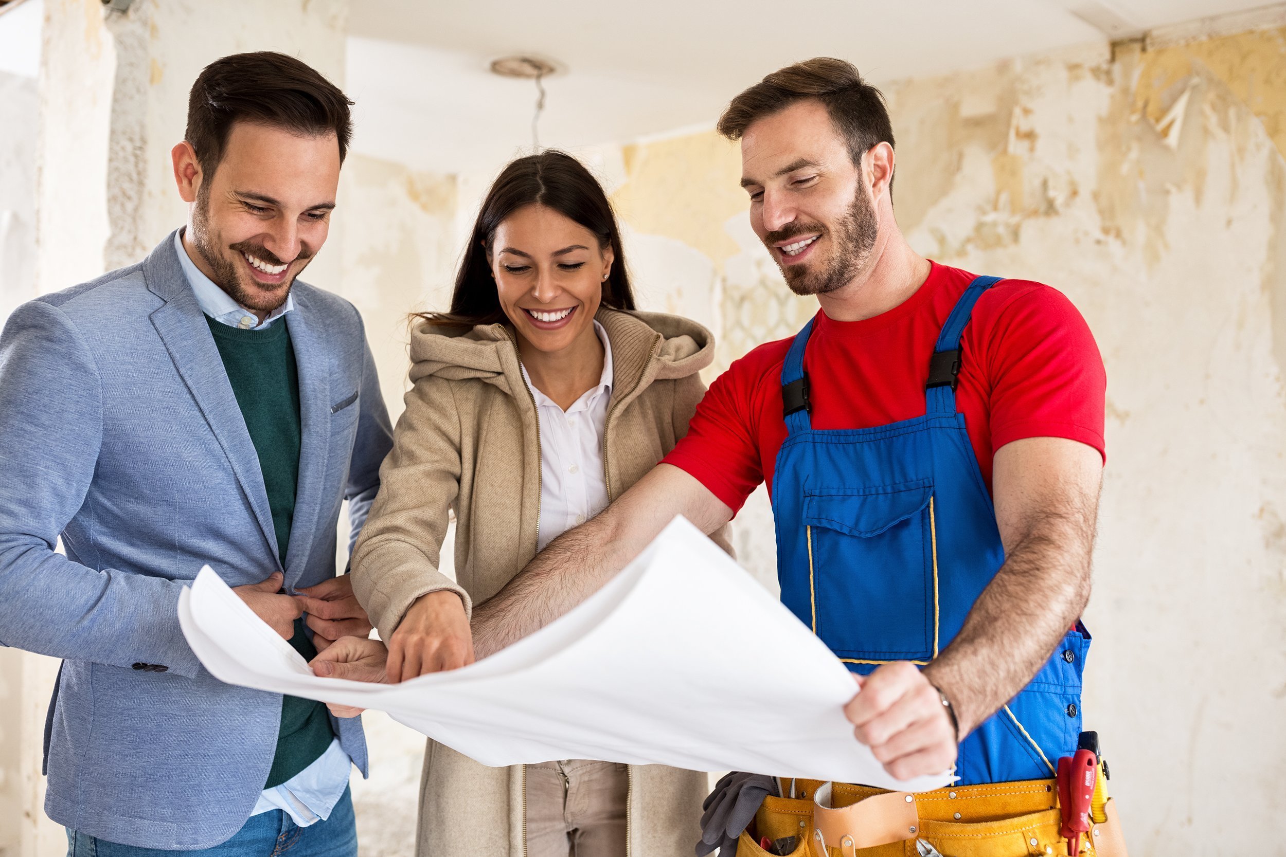 young couple looking blueprints of their home with handyman