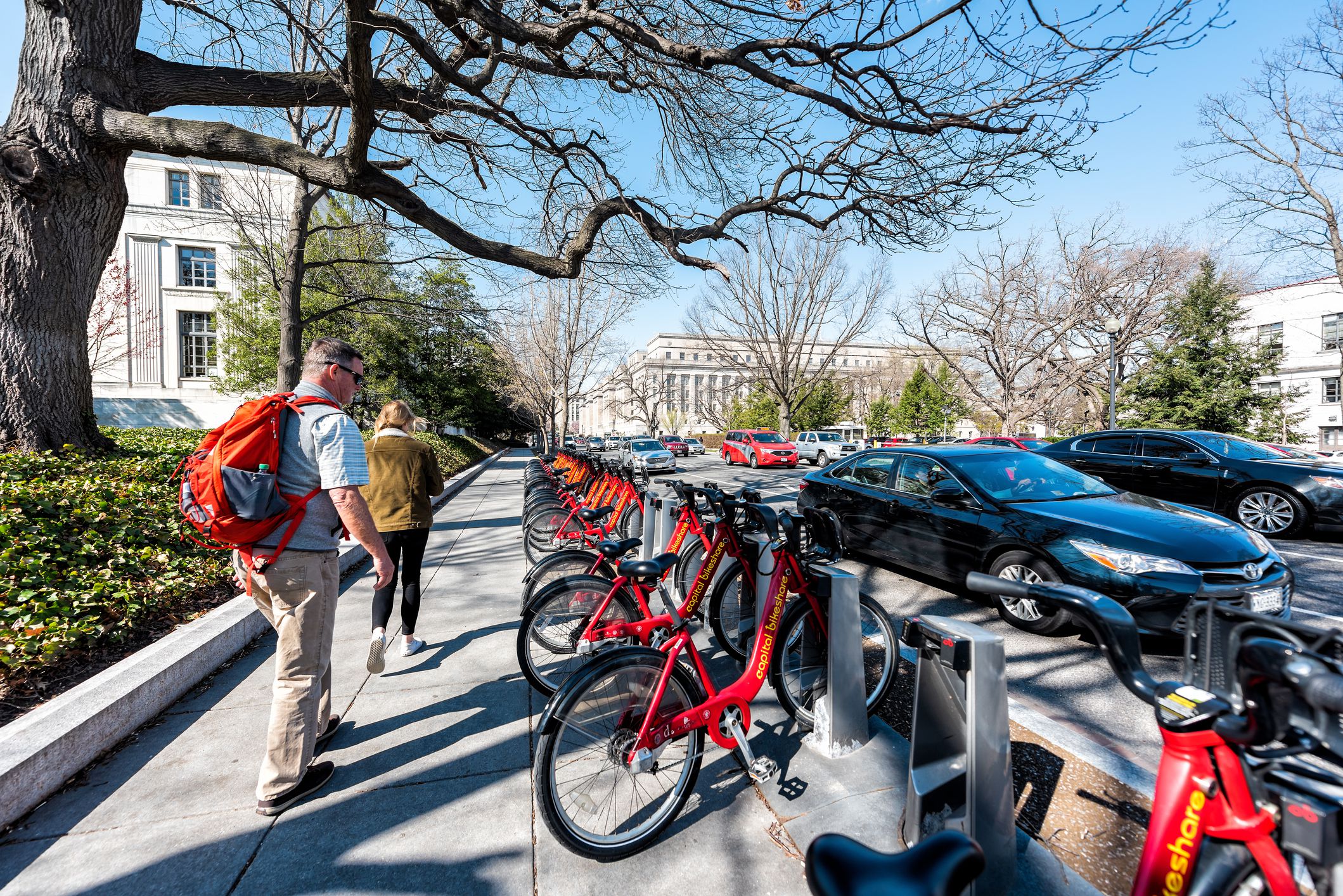 Capital bikeshare red bicycles row on sidewalk street in capital city, couple people walking, wide angle, road