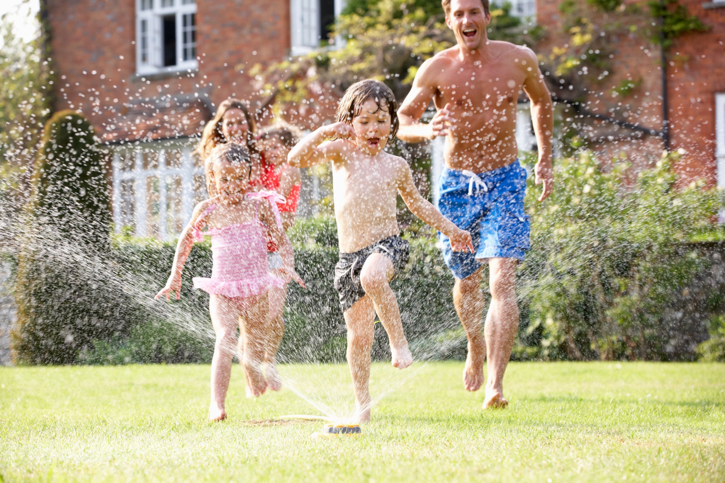 Family running through garden sprinkler