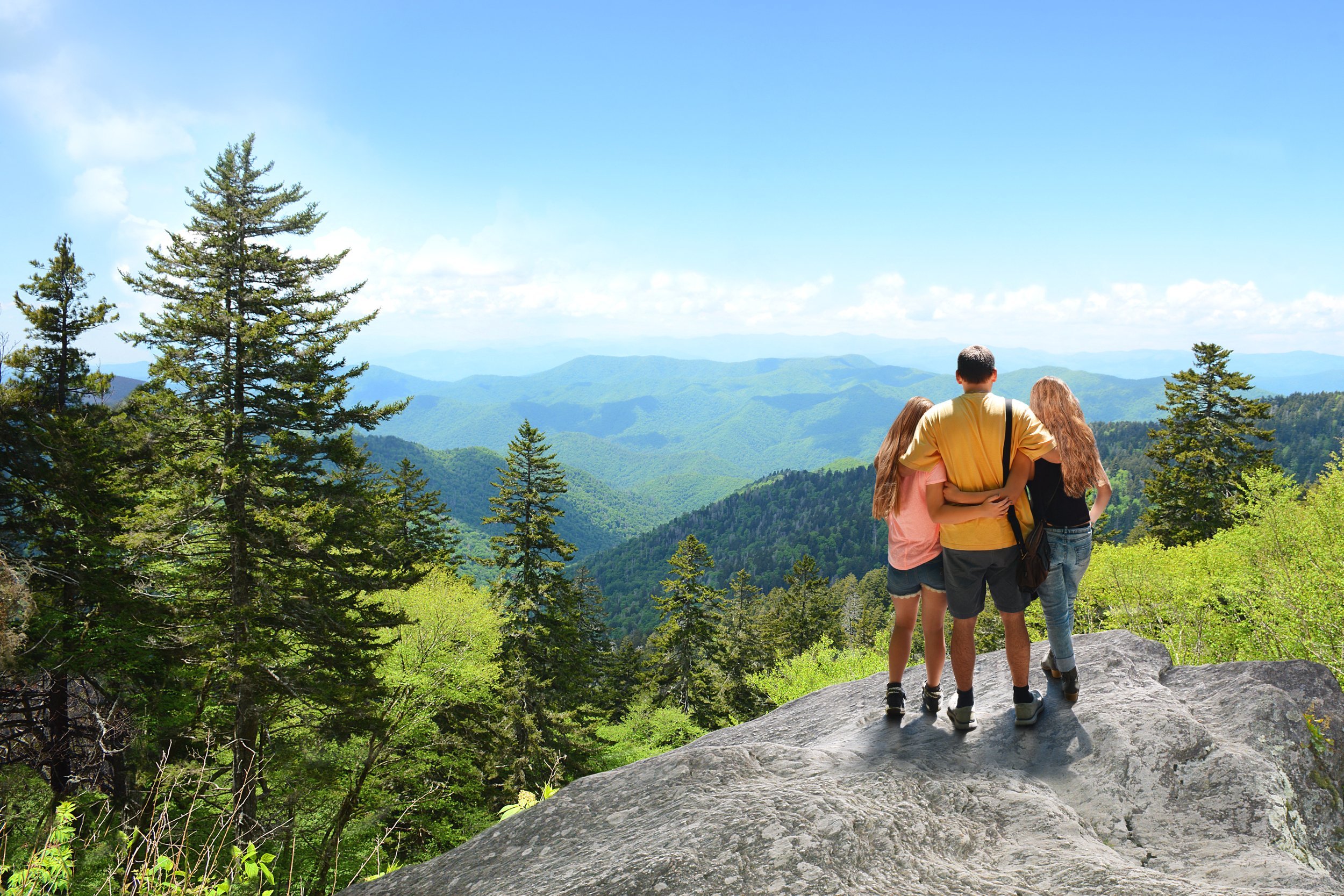 Family hiking on vacation, standing with arms around on top of the mountain