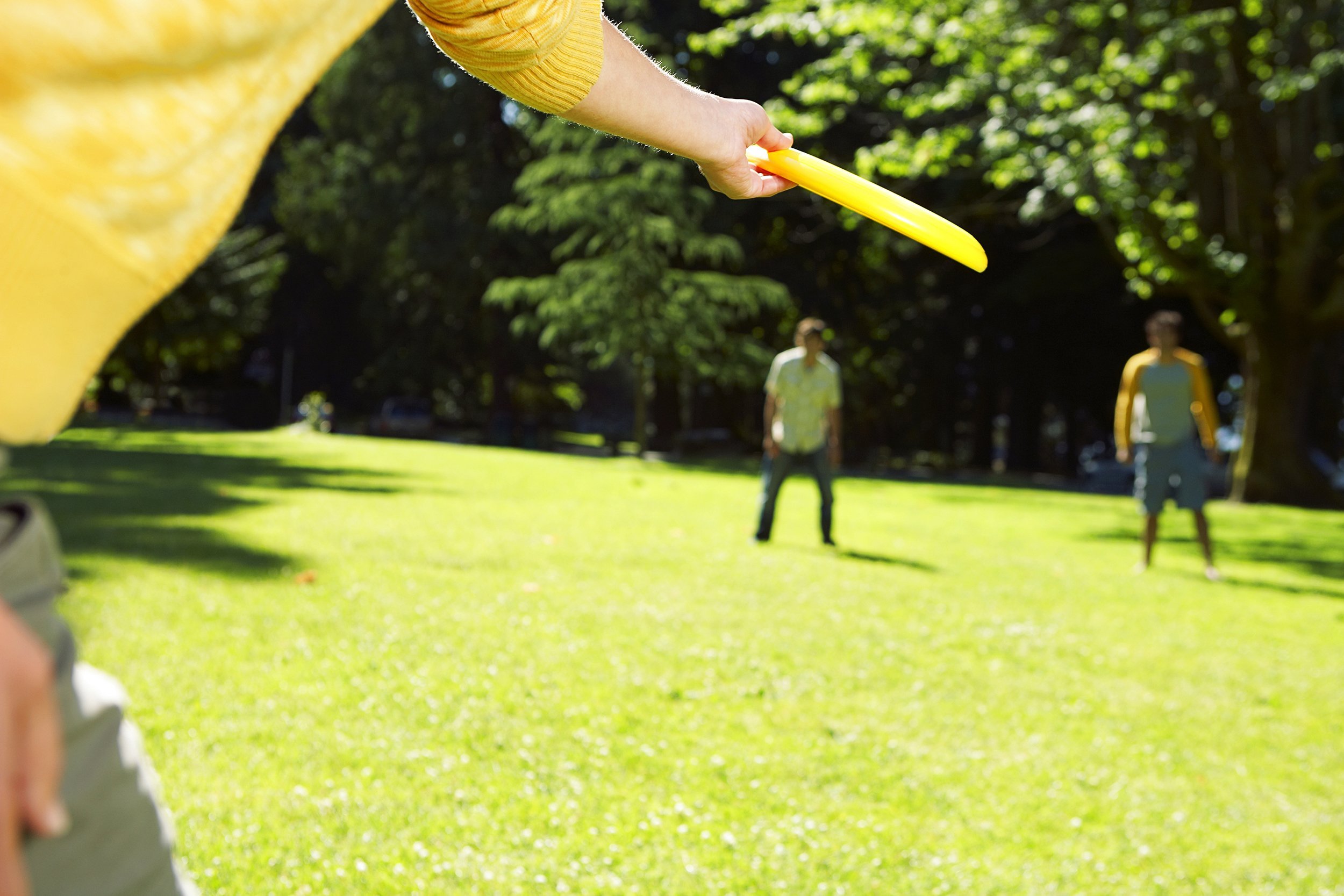 hand about to throw a frisbee to two people at the background
